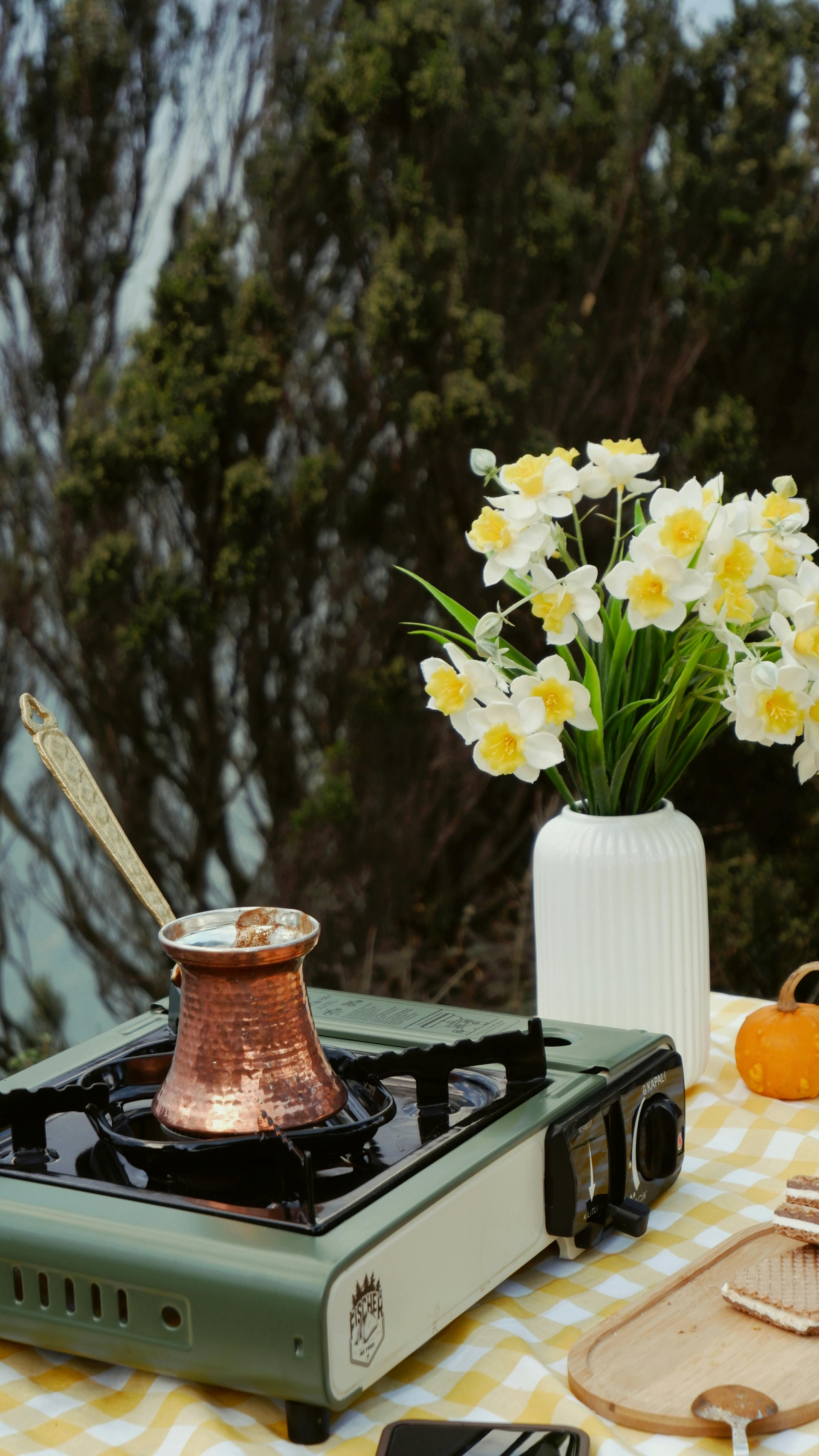 Gratis En kobberkanne som brygger kaffe utendørs ved siden av påskeliljer og gresskar. Arkivbilde