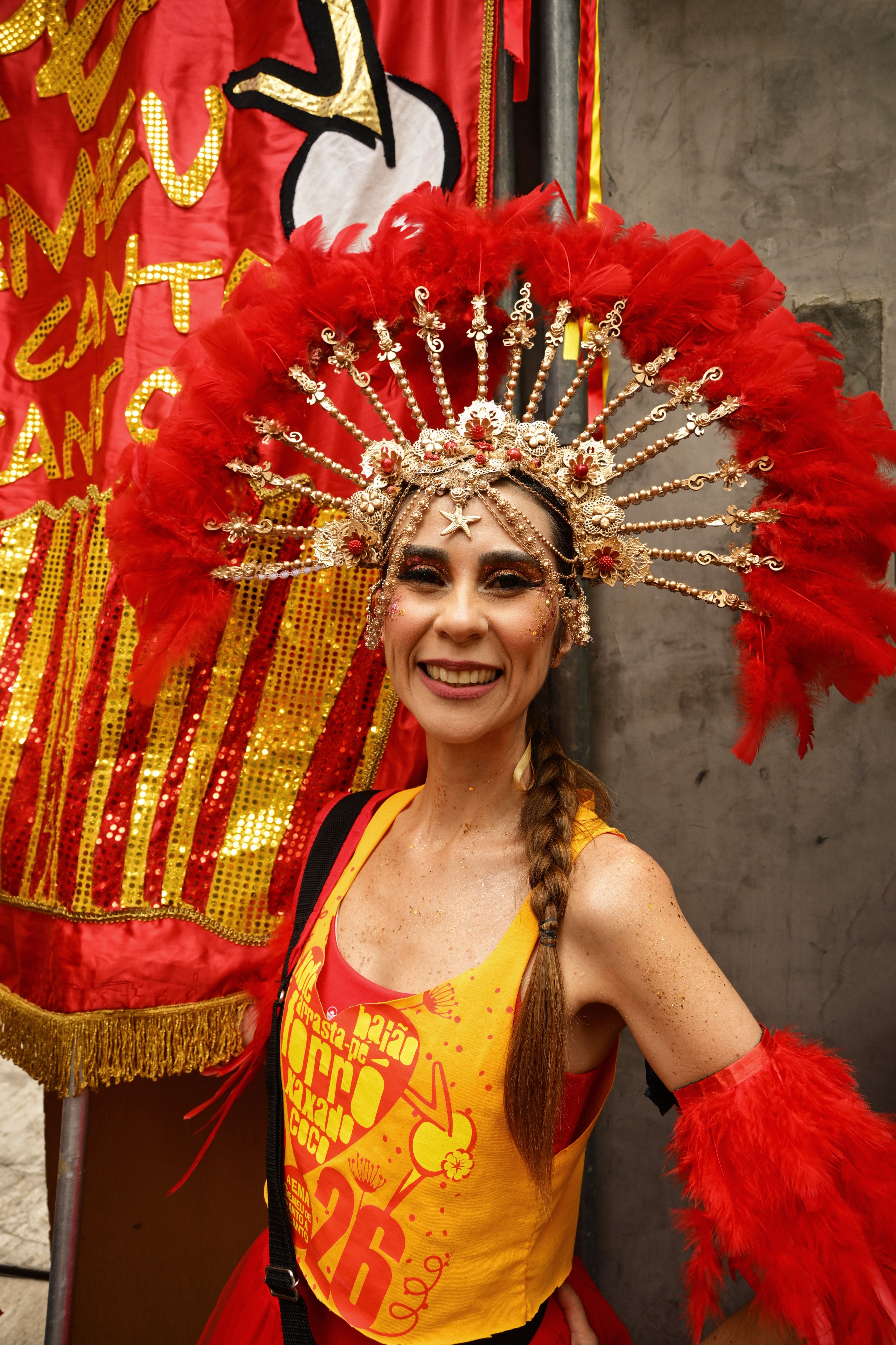 Carnival performer in a vibrant feathered costume smiling during a festive outdoor celebration.