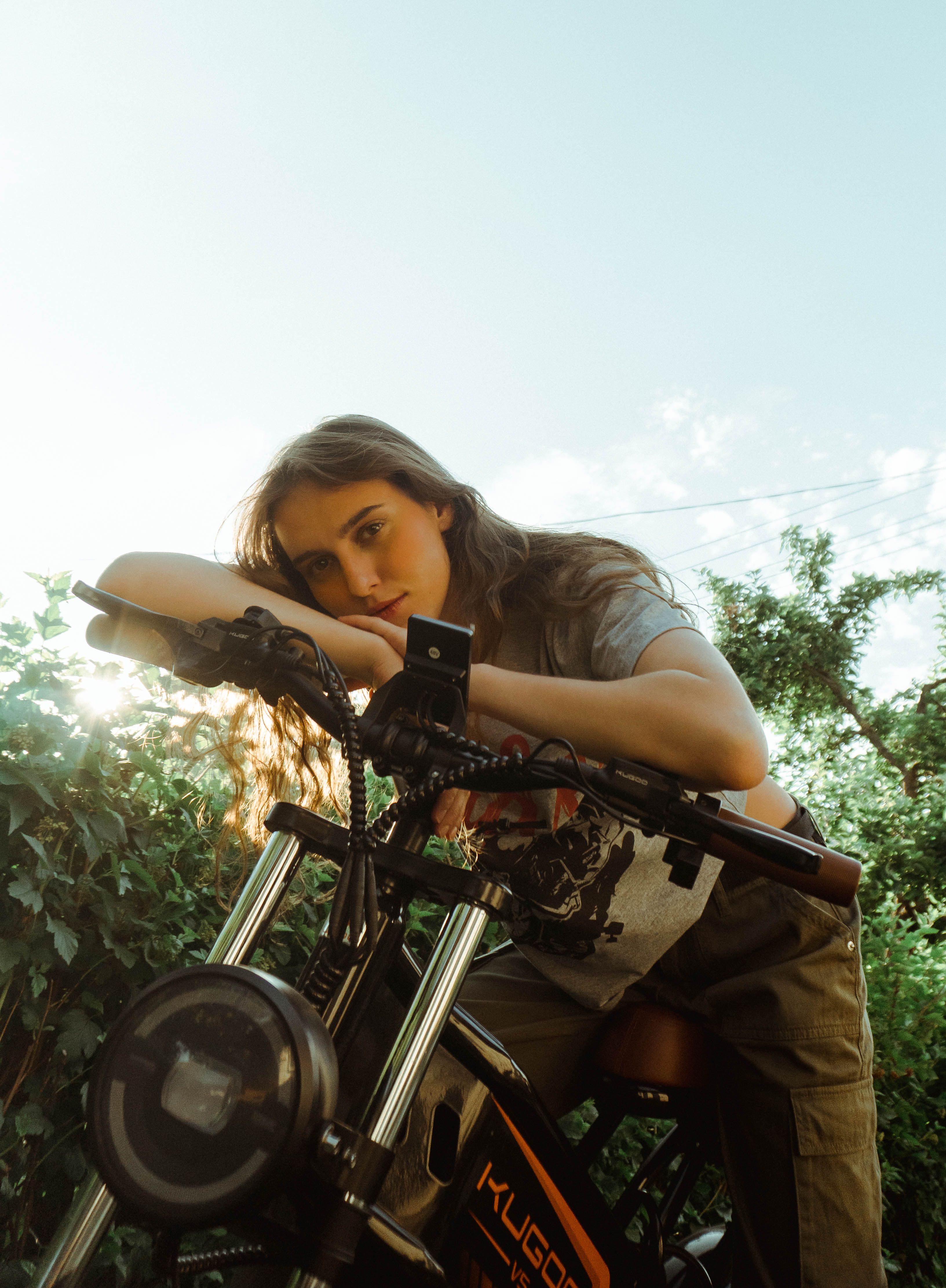 Young woman posing with a modern motorcycle outdoors under a clear blue sky.
