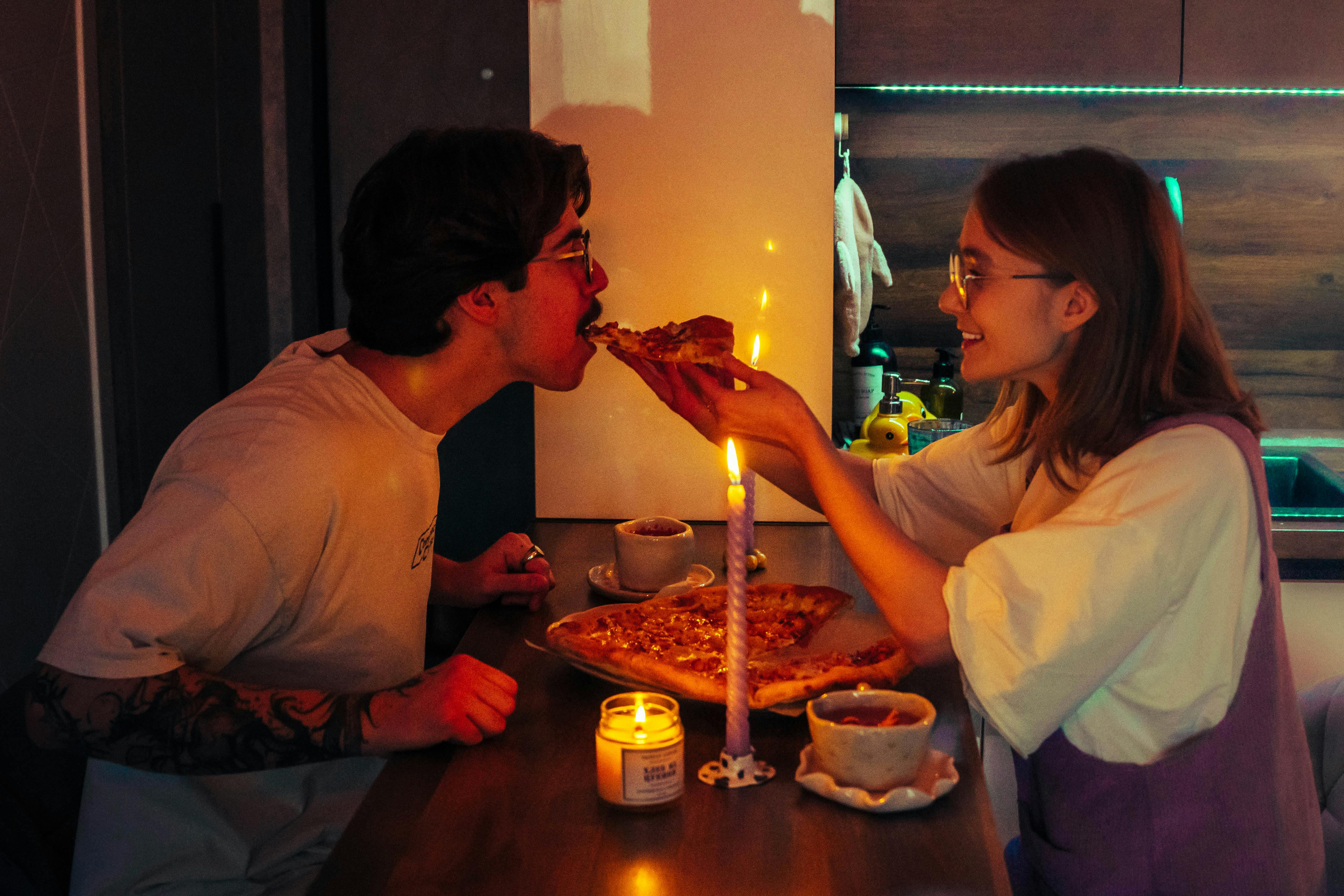 Gratis Pasangan ini menikmati makan malam pizza romantis dengan cahaya lilin di dapur yang nyaman. Foto Stok