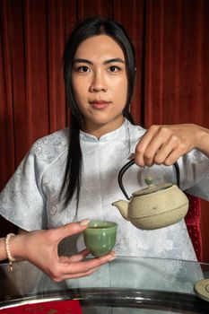 An Asian woman pouring tea from a ceramic teapot into a cup, showcasing cultural tradition in Chicago.