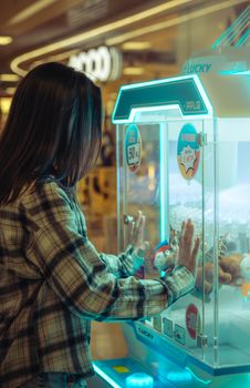 A teenager in a plaid shirt enjoys playing a claw machine at an indoor arcade.