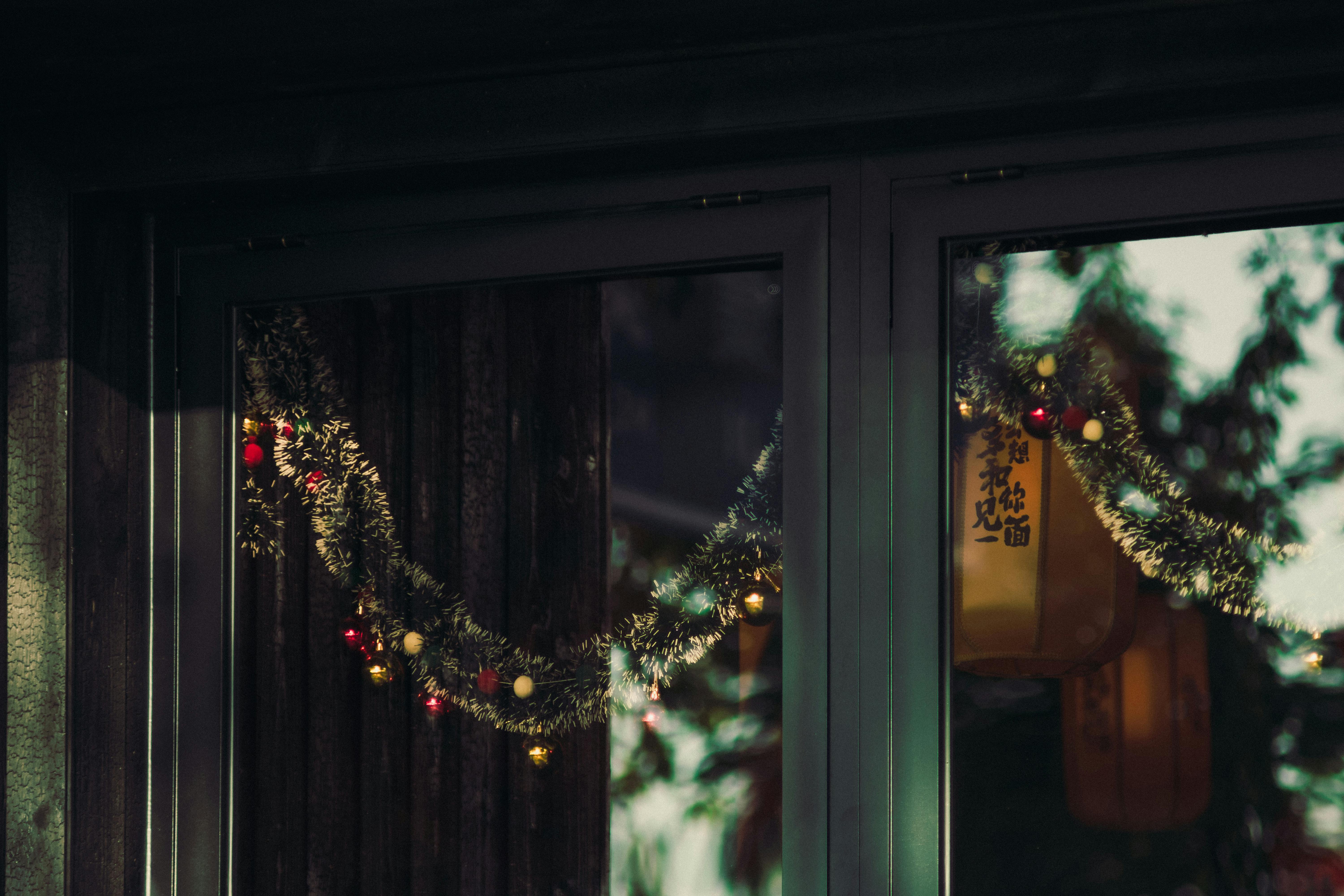Free Christmas garland with colorful lights reflecting in a window, capturing holiday vibes. Stock Photo