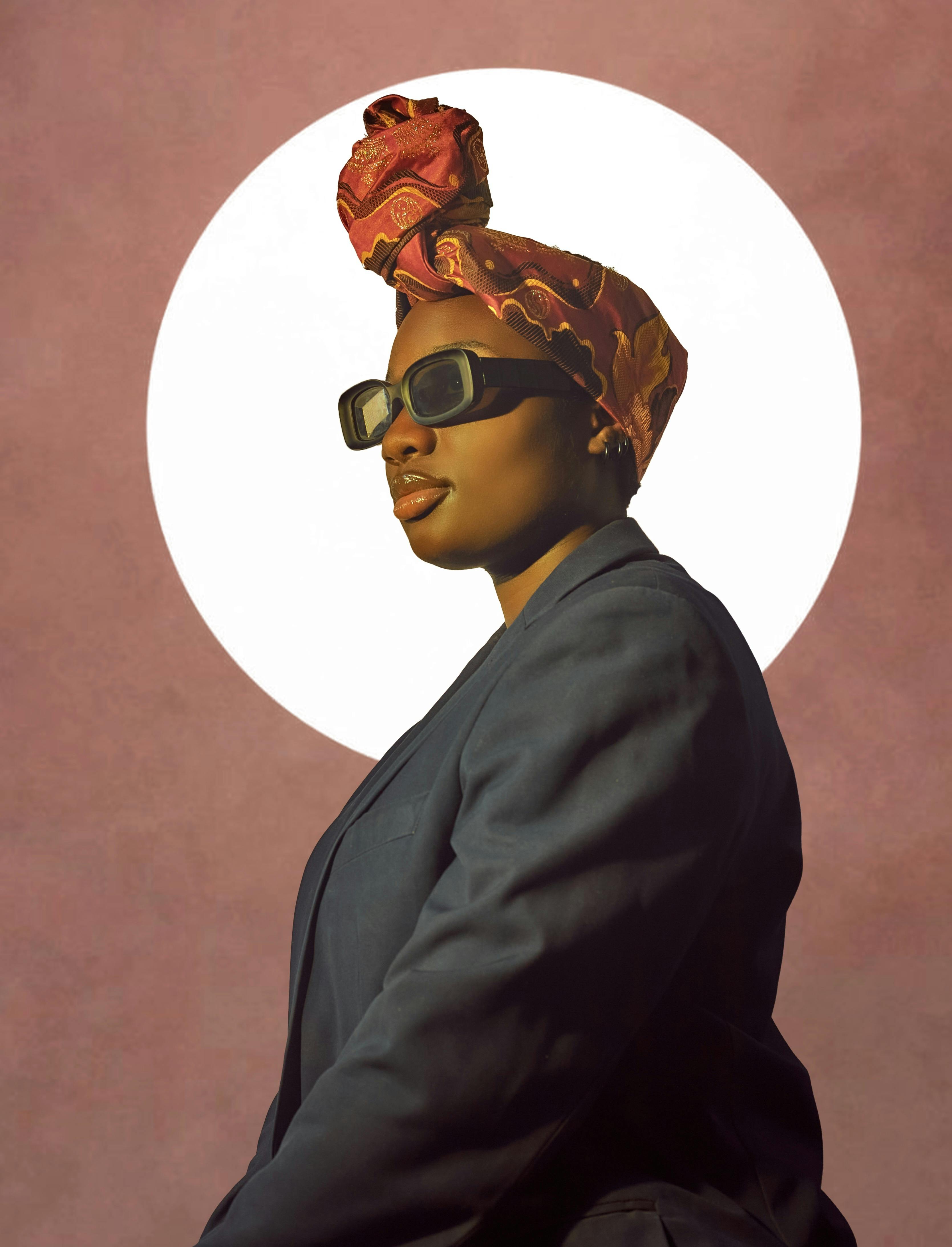 Free Elegant portrait of a woman in sunglasses and a headwrap against a pink backdrop. Stock Photo