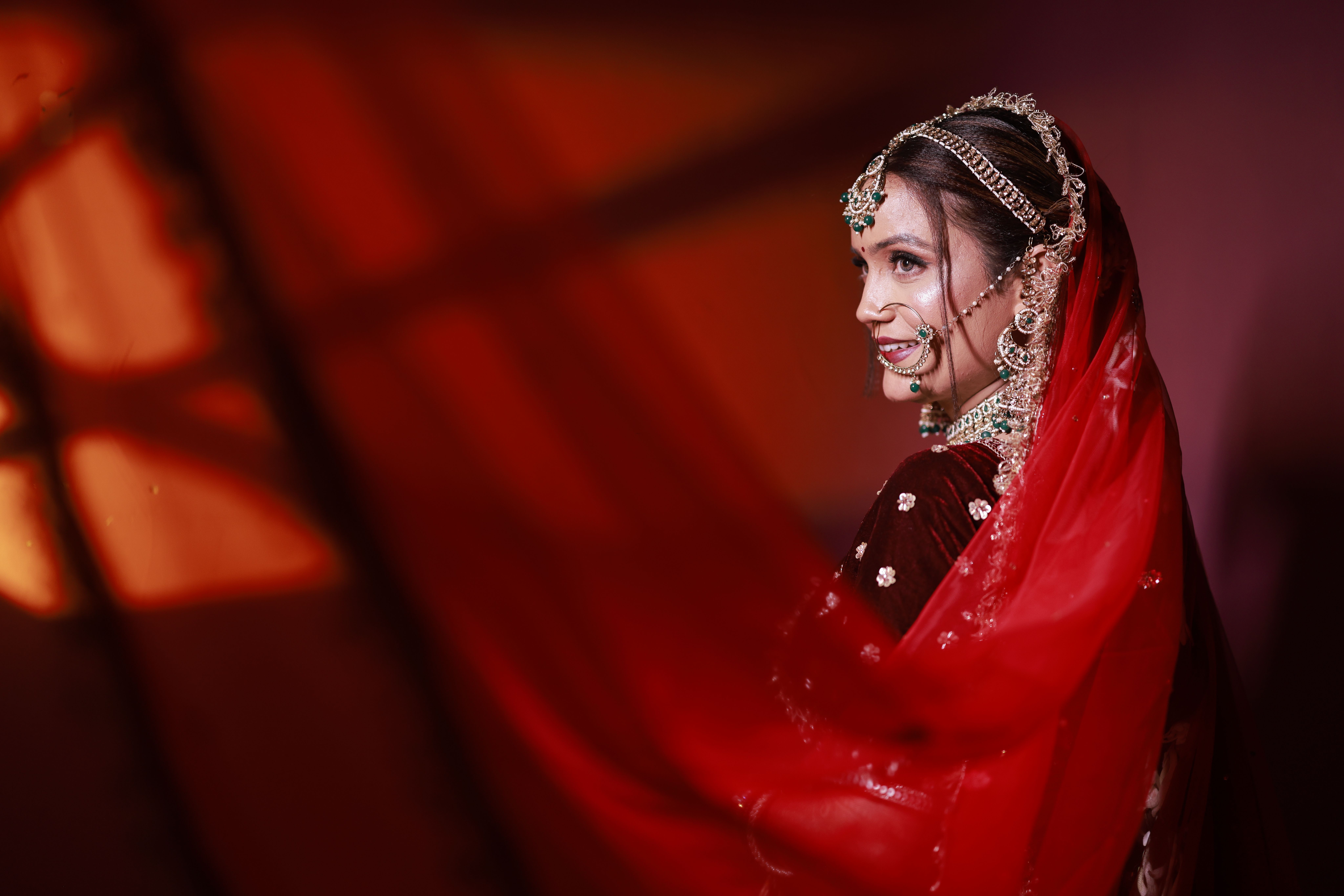 Beautiful Indian bride in red saree adorned with intricate jewelry and striking makeup.
