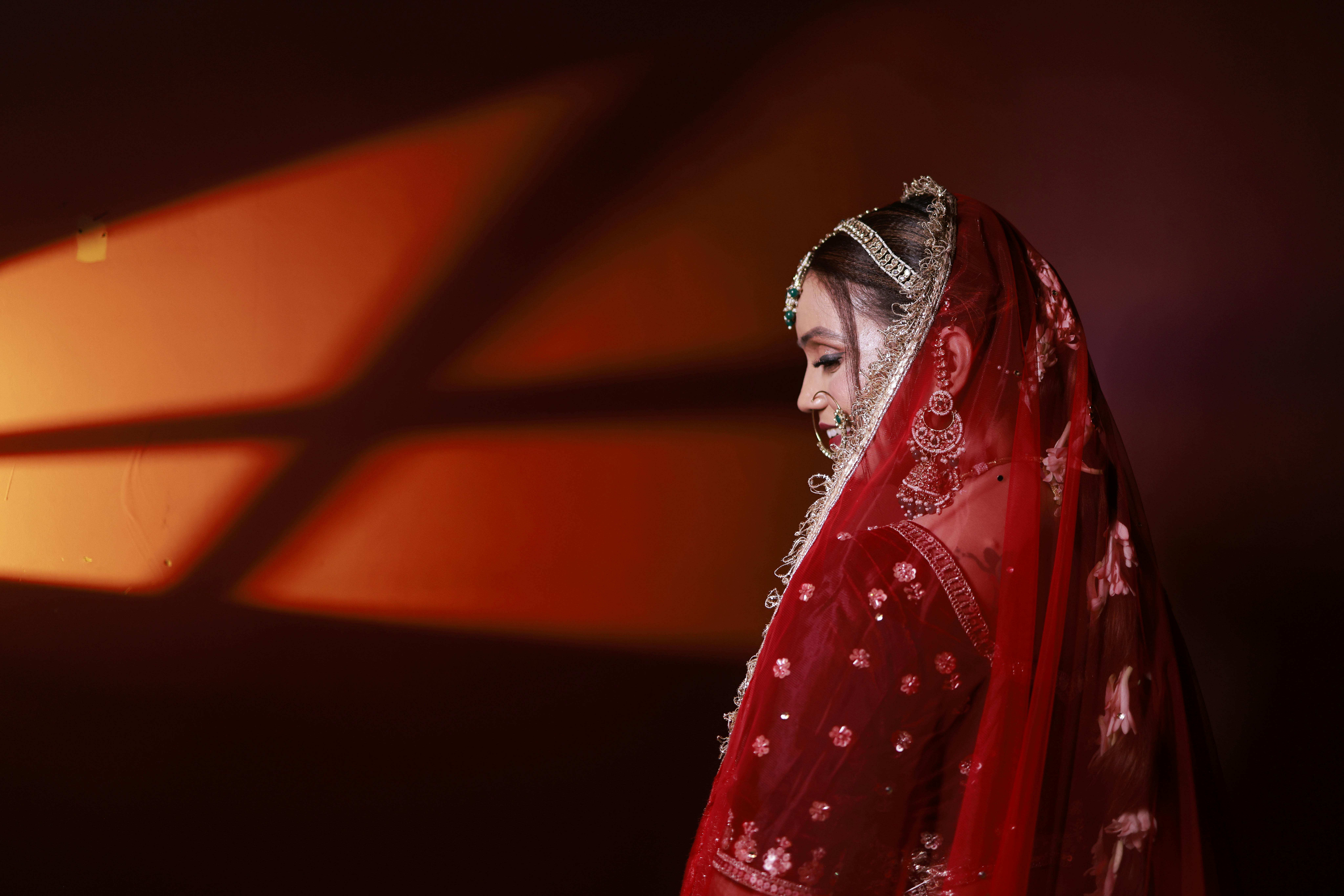 Gratis Splendida immagine di una sposa in abito tradizionale rosso, artisticamente illuminata con colori caldi. Foto a disposizione