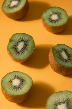 Sliced kiwi fruits on a bright yellow surface showcasing their vivid green color and texture.