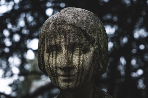 Free Close-up of an aged stone statue with moss, set against a gloomy forest backdrop. Stock Photo