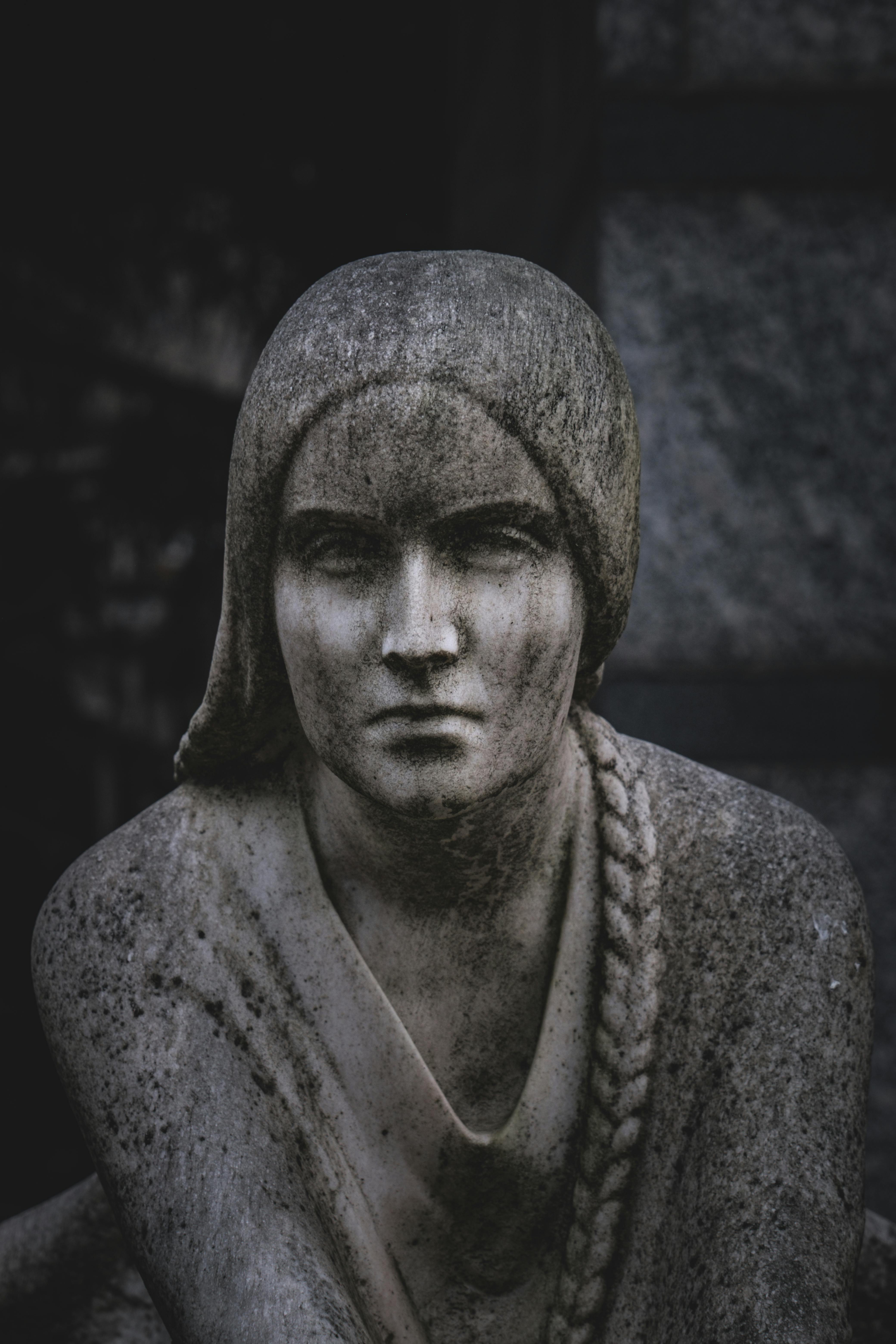 Free A close-up of a solemn stone sculpture depicting a woman with braided hair. Stock Photo