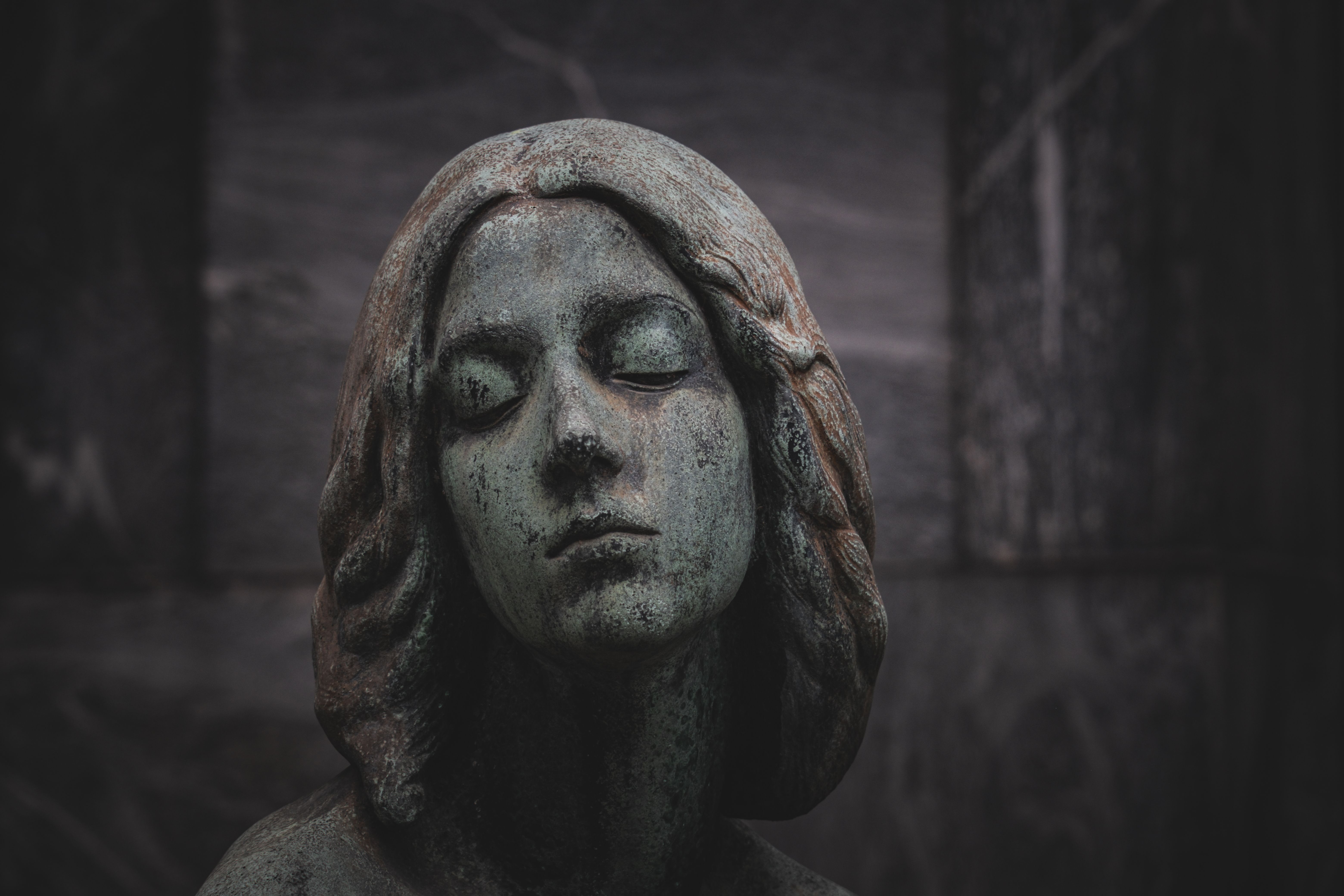 Close-up of a serene stone statue with a green patina finish, set against a dark background.
