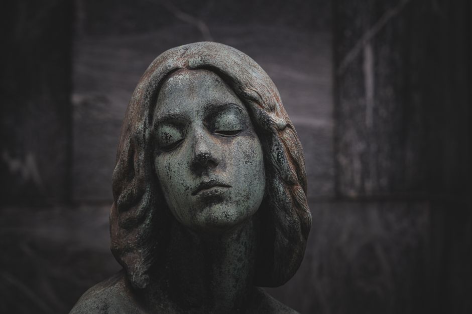 Close-up of a serene stone statue with a green patina finish, set against a dark background.