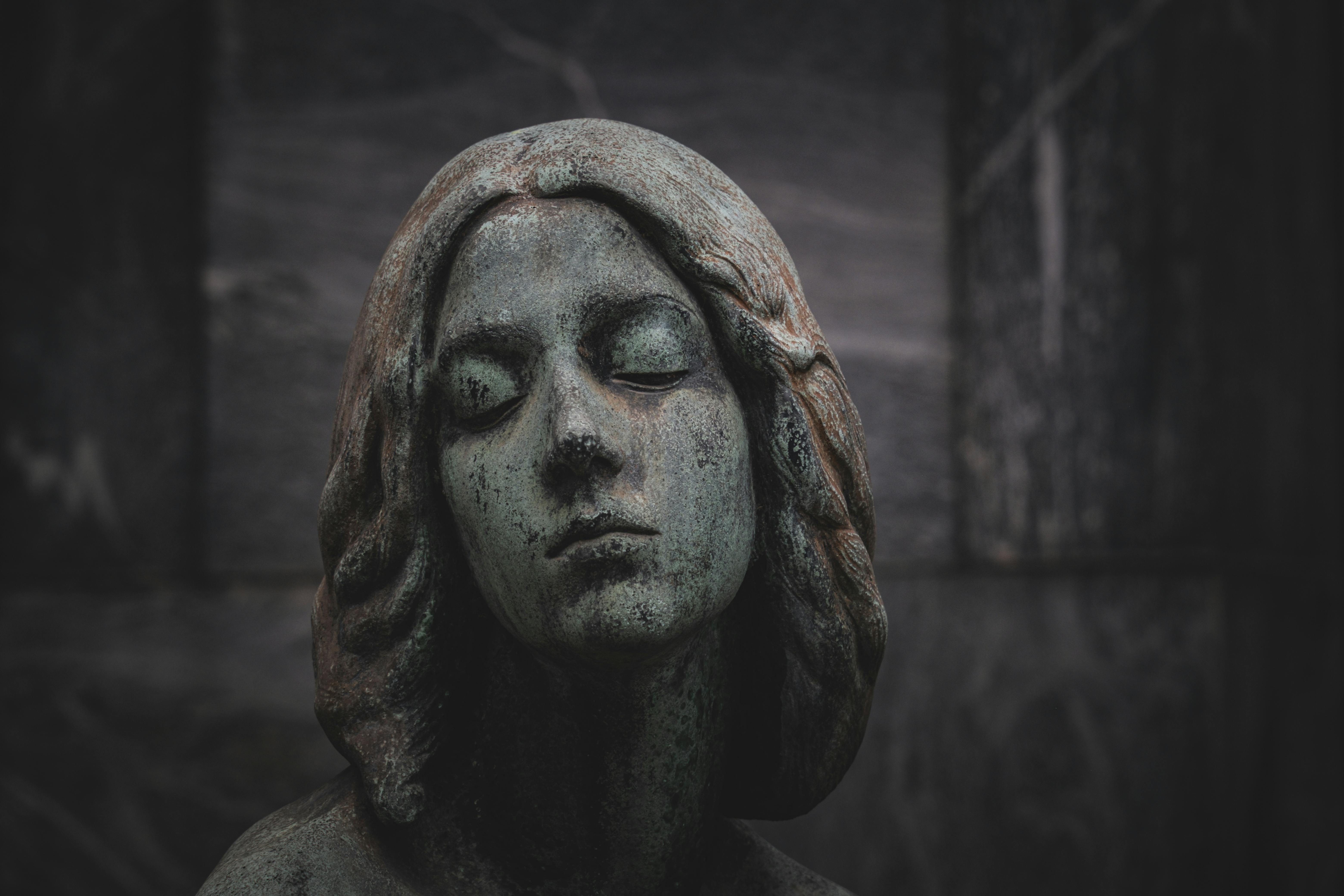 Free Close-up of a serene stone statue with a green patina finish, set against a dark background. Stock Photo