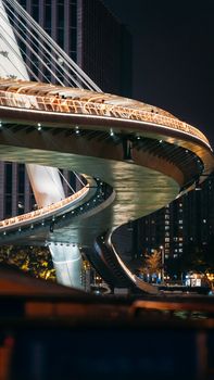 A striking view of a modern cable-stayed bridge illuminated at night, with urban architecture.