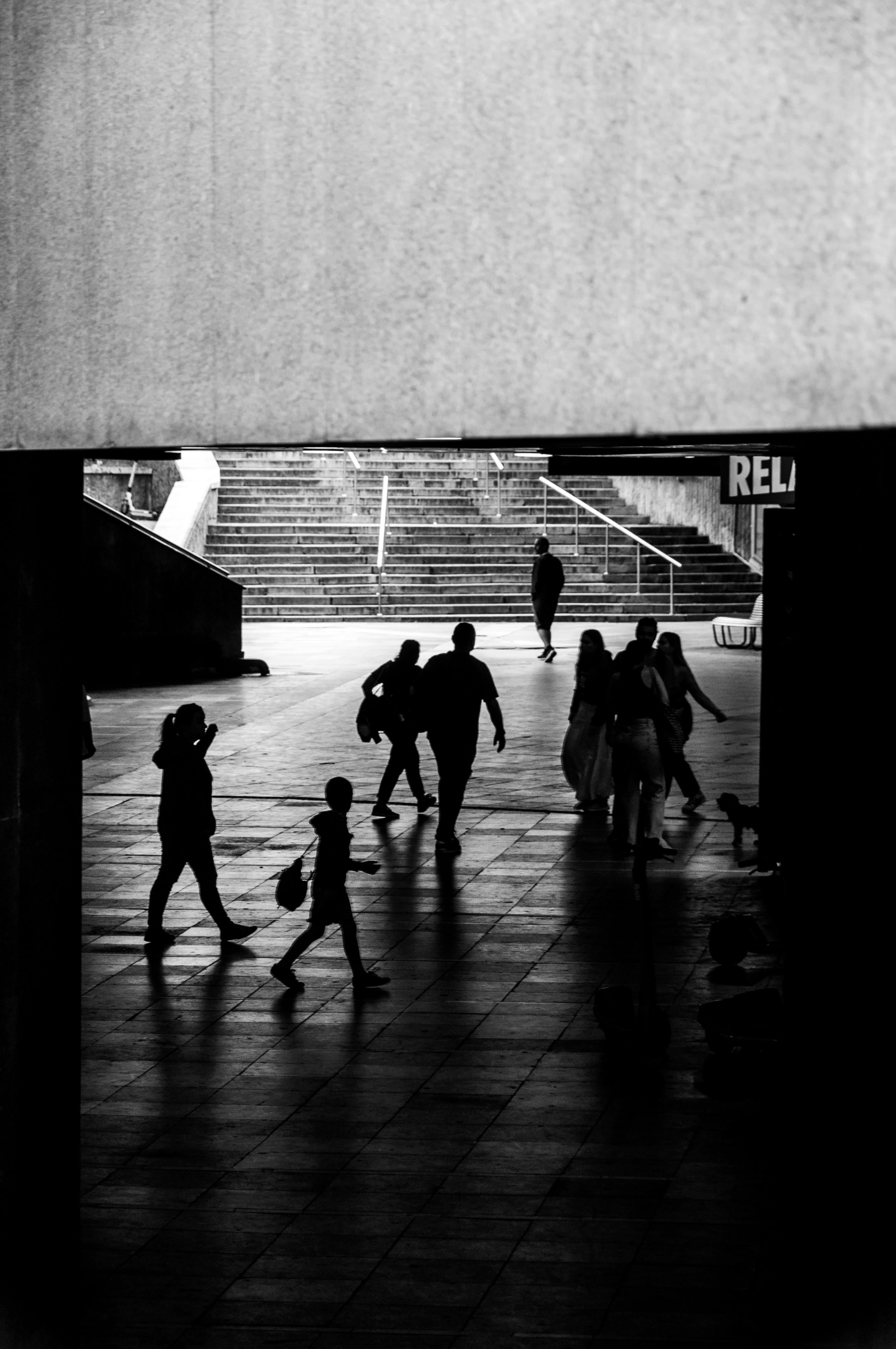бесплатная Черно-белая сцена, изображающая людей, идущих по городскому подземному переходу, с акцентом на тени и движение. Стоковое фото