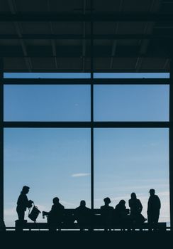 Silhouettes of people sitting and standing in an airport terminal with a large window view.
