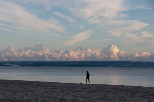 Free A person walks along a serene beach during dusk. Dramatic clouds enhance the peaceful ambiance. Stock Photo