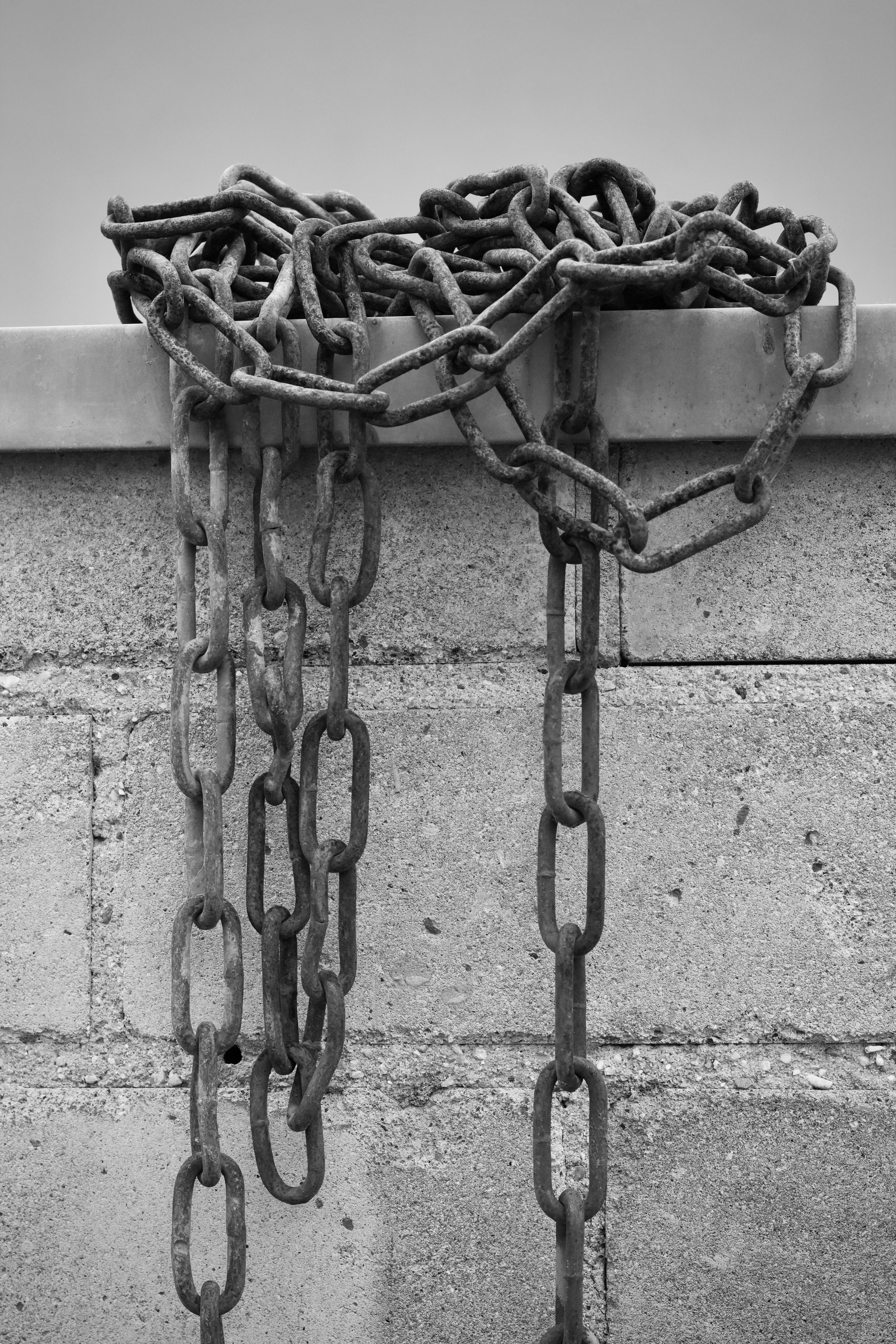 Black and white photo of rusted chains hanging from a concrete wall, creating an industrial ambiance.