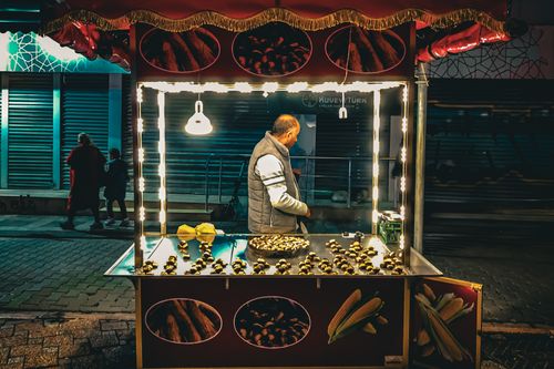 Free Street vendor selling roasted chestnuts under bright lights on a night street scene. Stock Photo
