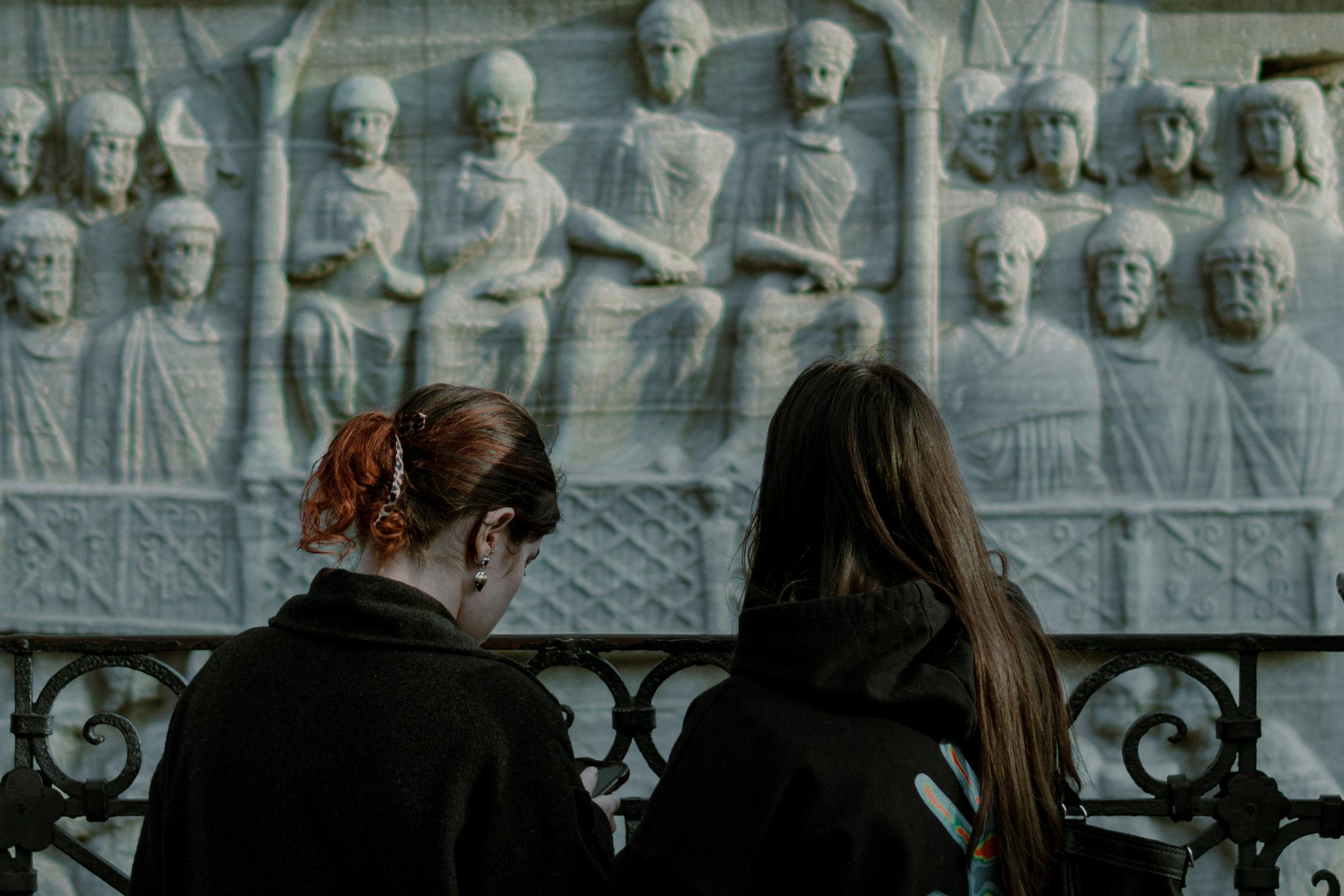 Two women viewing historic stone carvings depicting ancient figures, offering a glimpse into history.