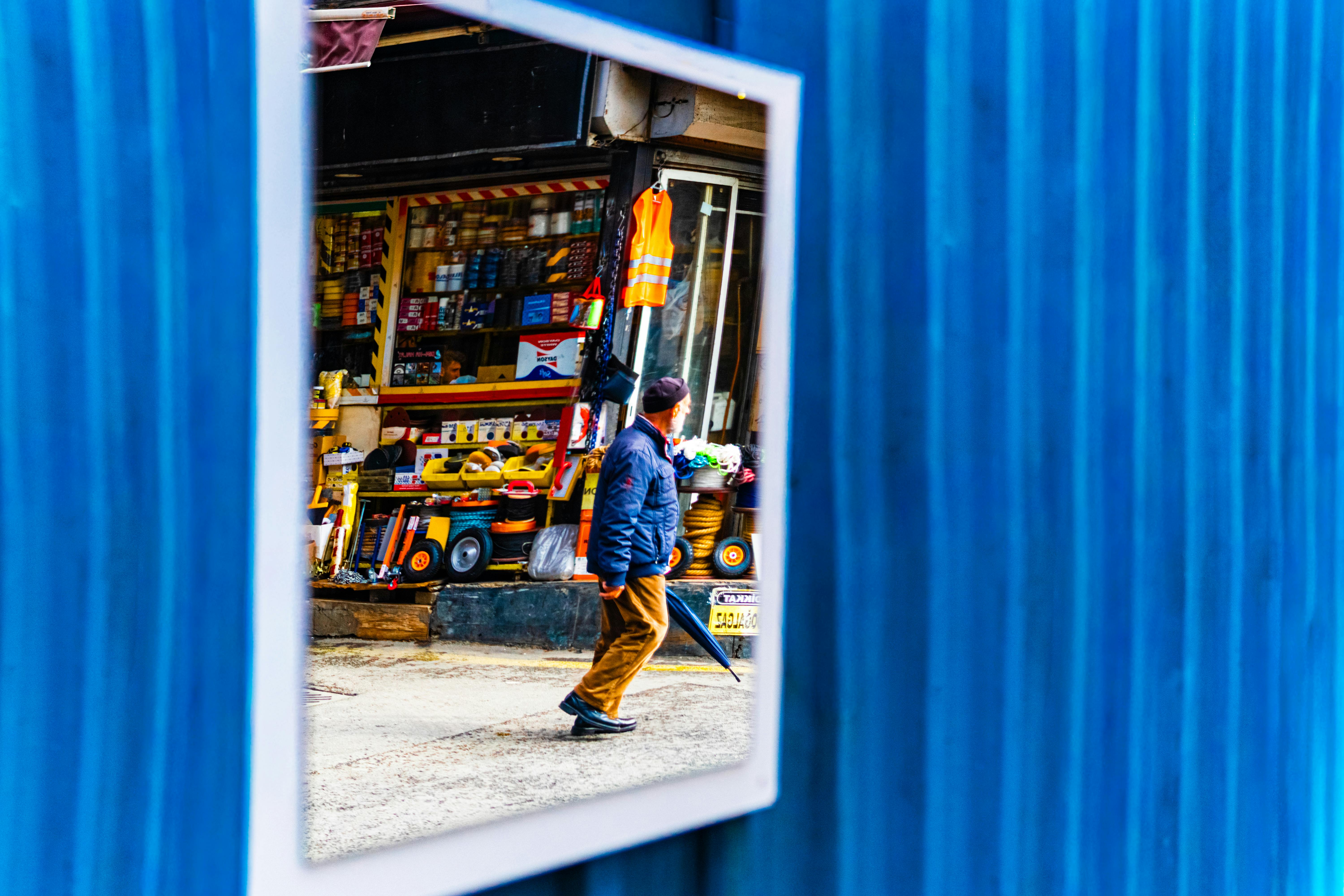 Free A man in a blue jacket is seen walking past a store, reflected in a mirror. Stock Photo