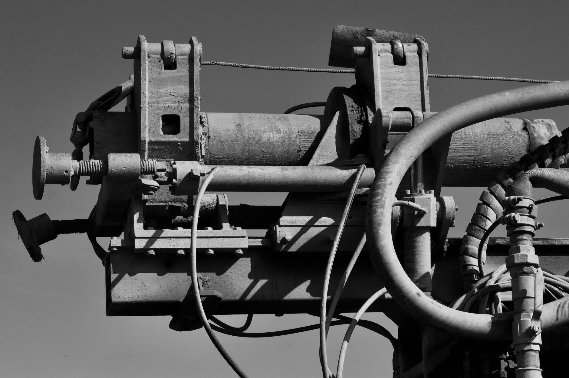 Detailed black and white image of industrial machinery with pipes and gears against a clear sky.