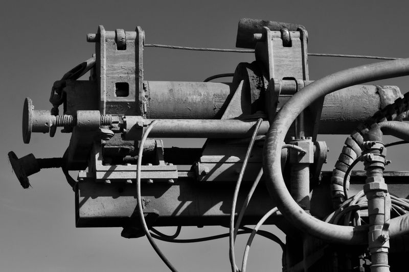 Detailed black and white image of industrial machinery with pipes and gears against a clear sky.