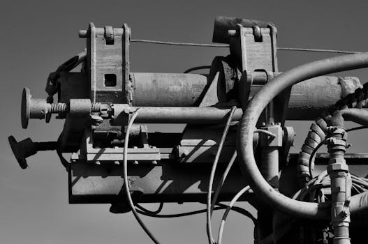 Detailed black and white image of industrial machinery with pipes and gears against a clear sky.
