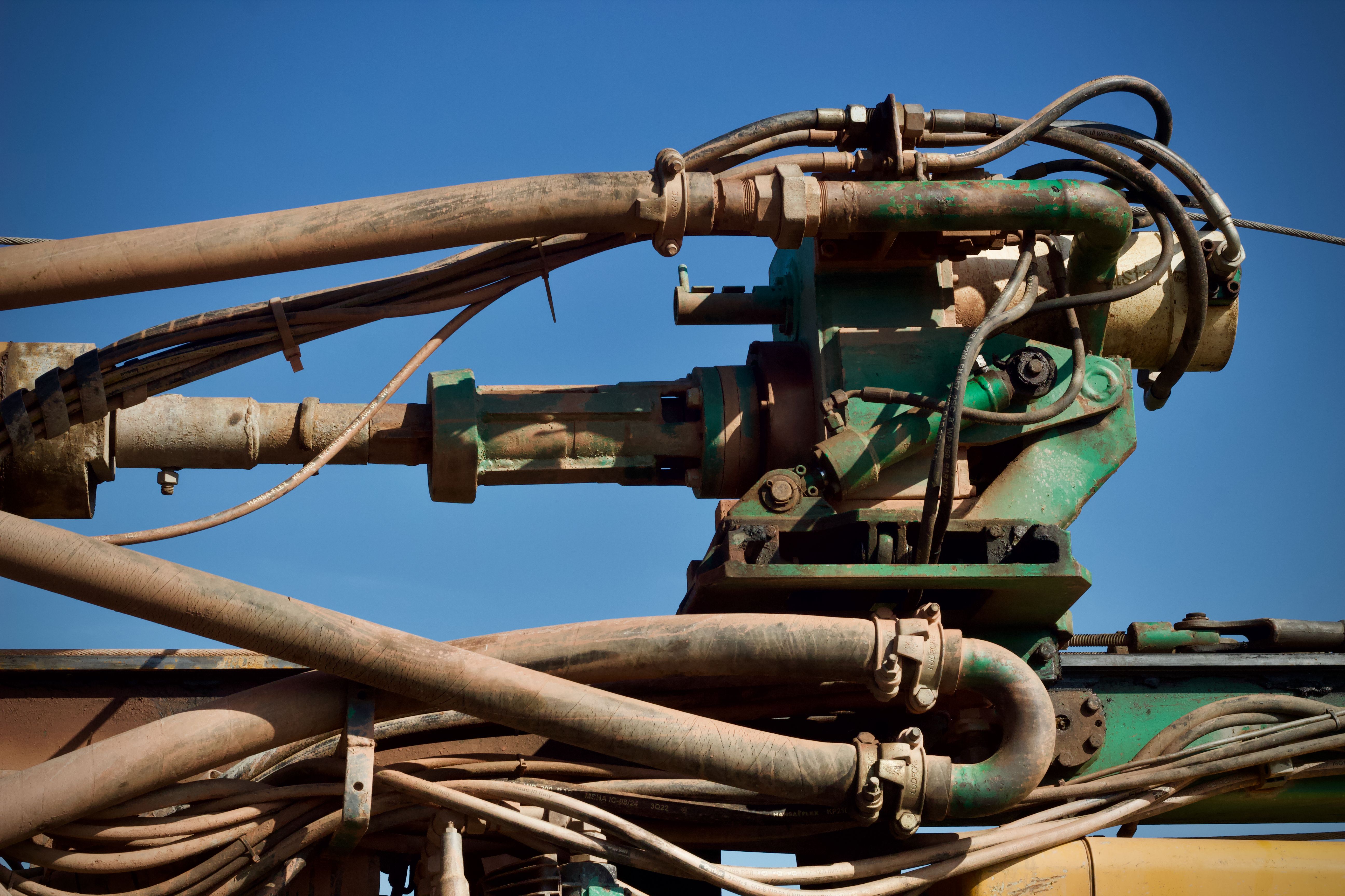 Imagem de uma estrutura de máquinas industriais e tubulações sob céu claro, representando o setor de engenharia ou manutenção de equipamentos pesados.