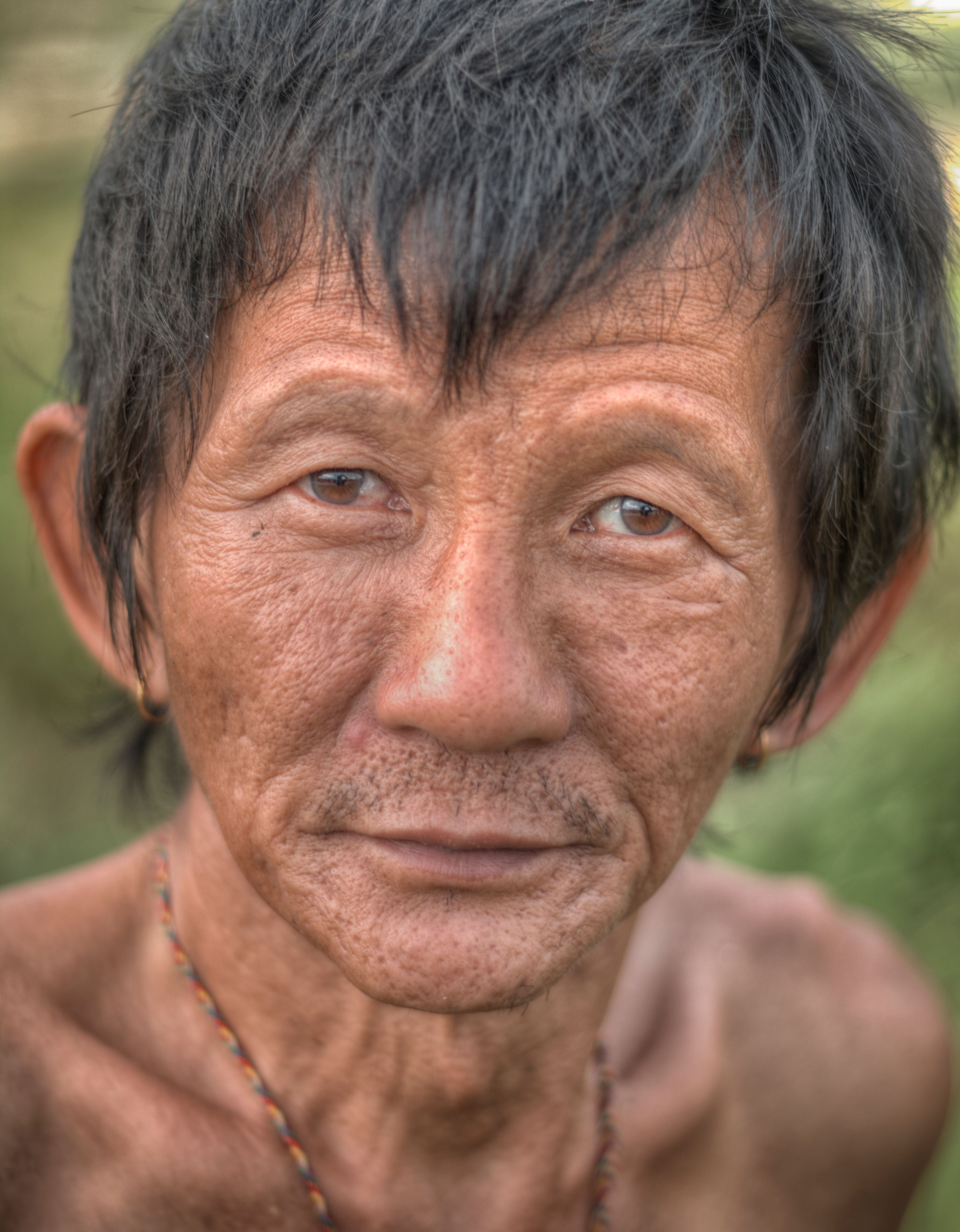 Detailed close-up portrait of an elderly man with rugged features and a serene expression outdoors.