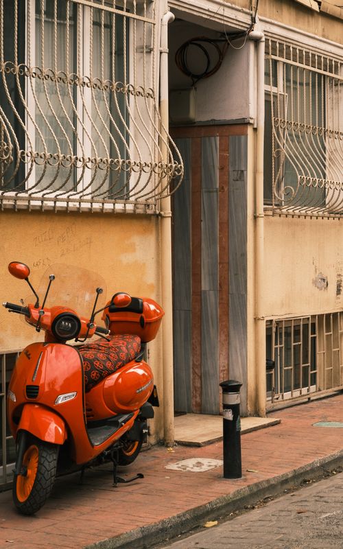 Free Orange scooter parked outside a vintage urban building, evoking city lifestyle and travel adventure. Stock Photo