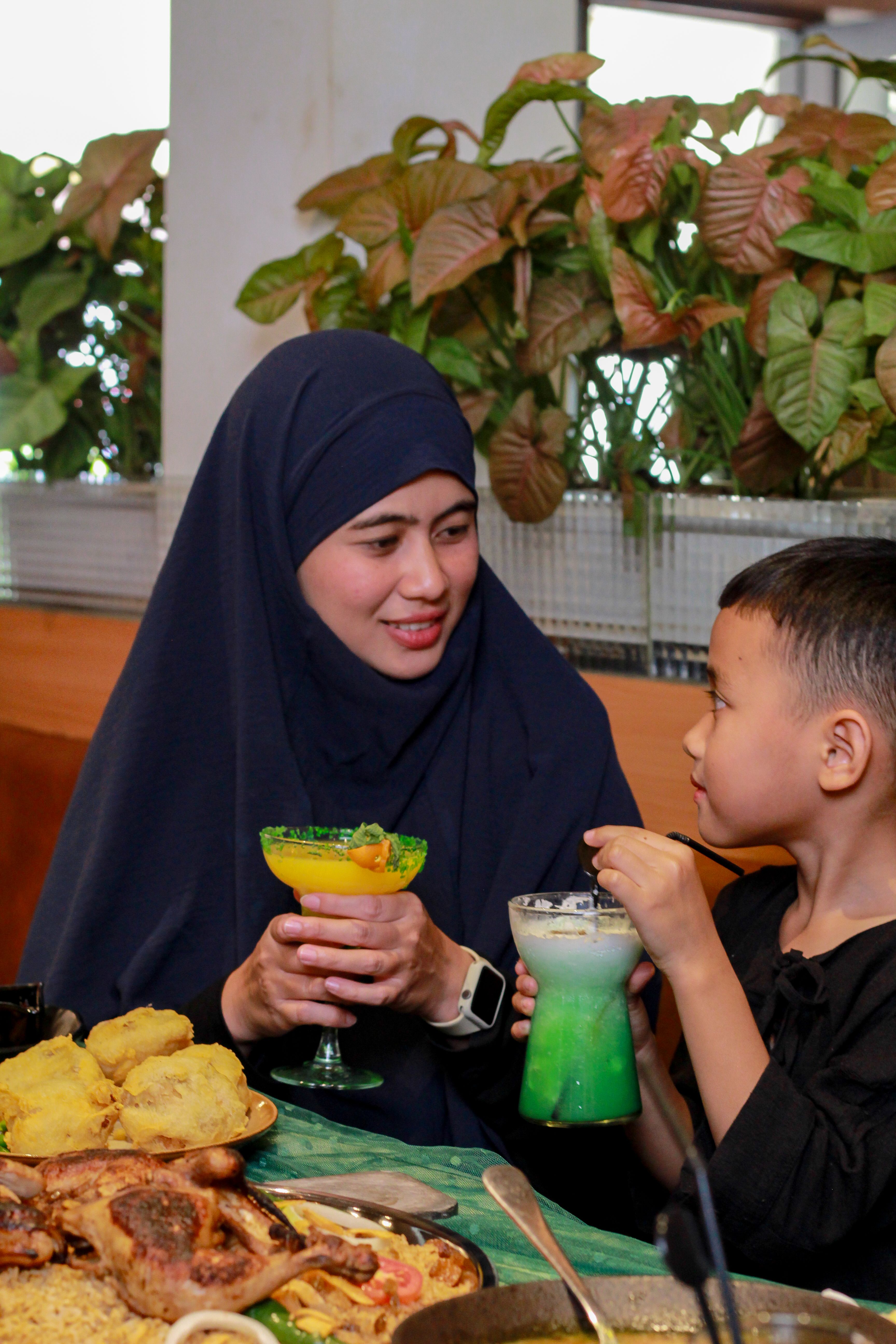 A mother and child enjoy a meal indoors with vibrant fruit drinks.