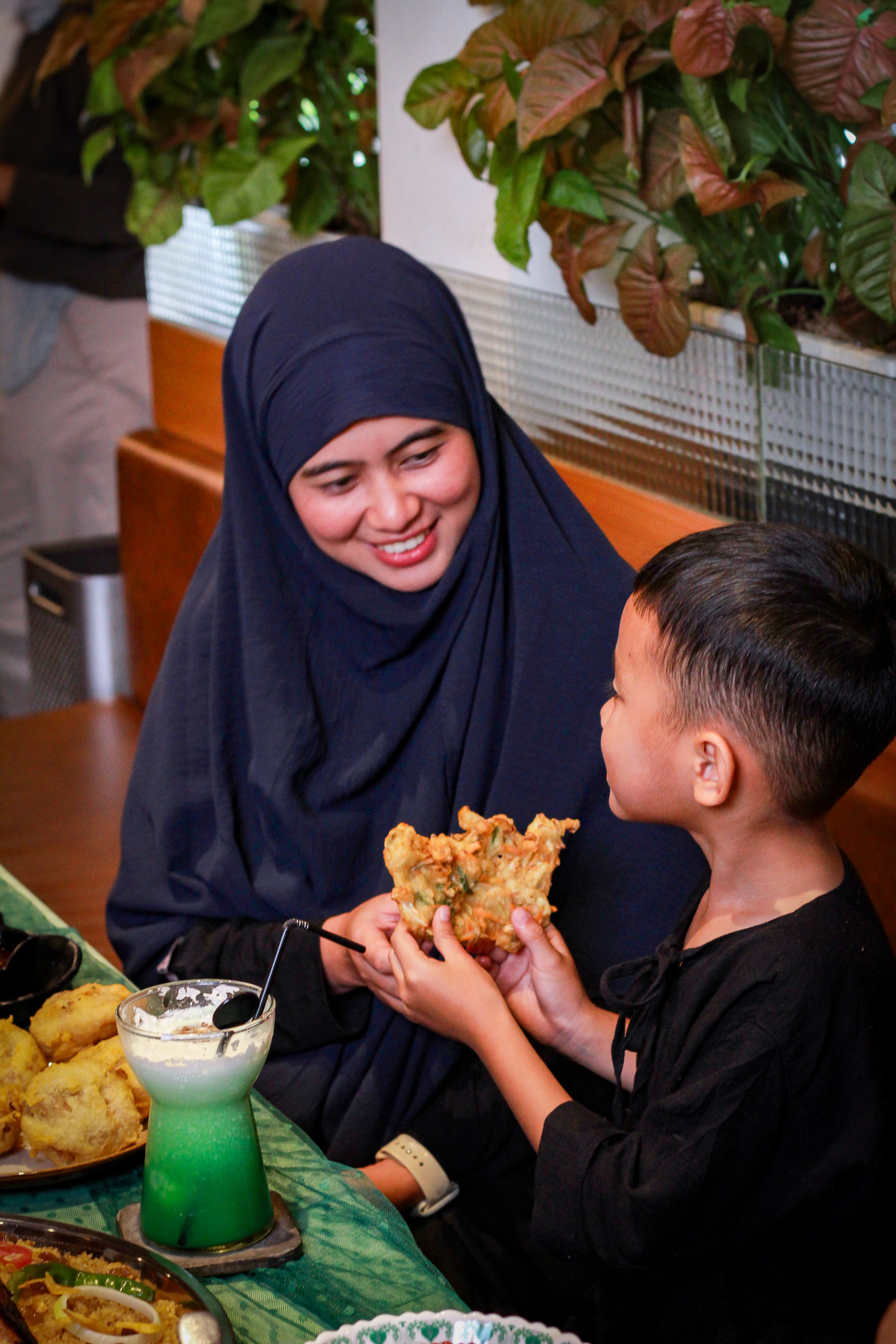 A smiling mother and son enjoying a meal with traditional Asian food and drinks, conveying happiness and family bonding.
