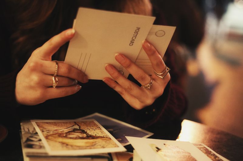 Close-up of a woman holding postcards at a cozy café. Warm, intimate setting.