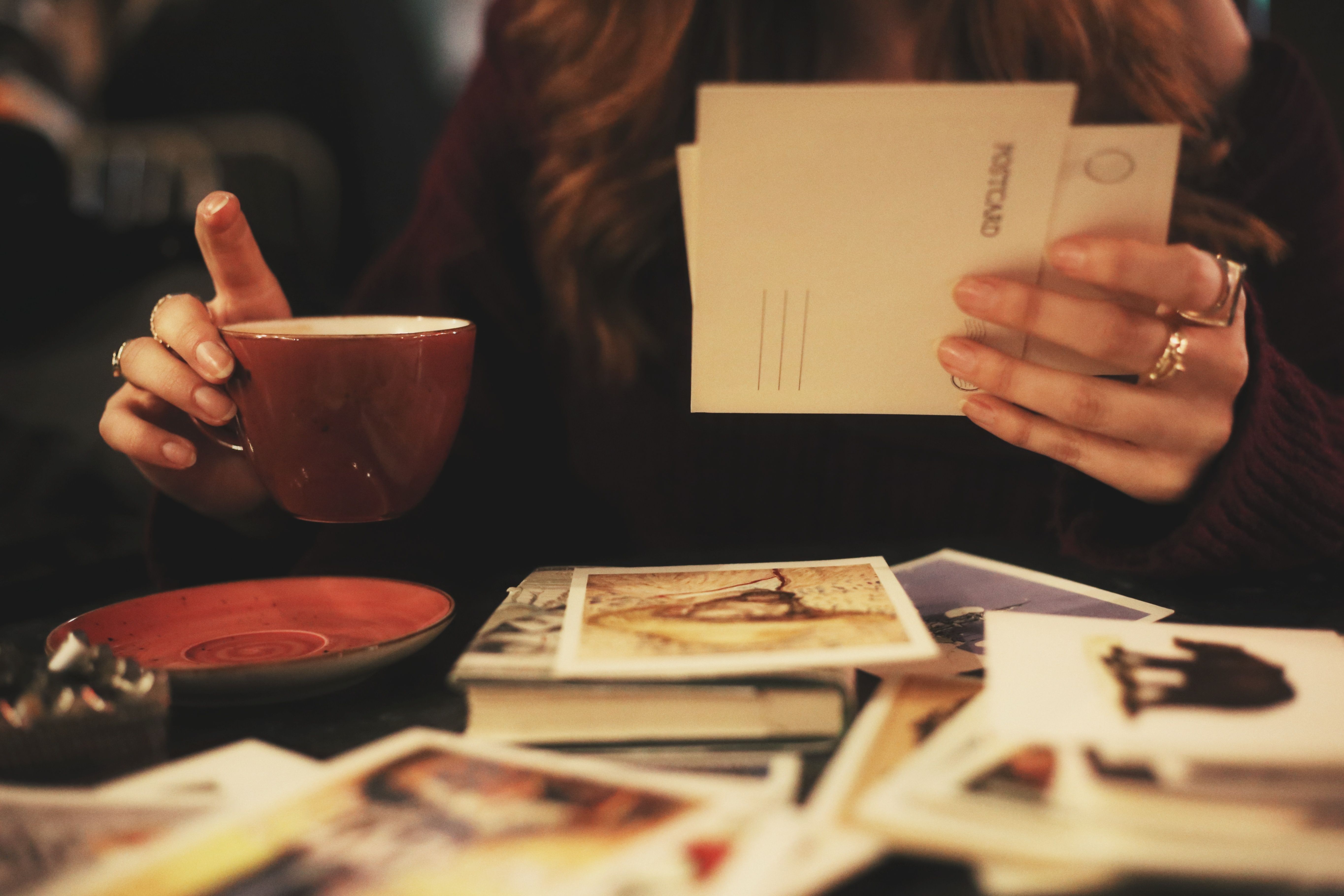 A woman holding postcards while sipping coffee, a cozy indoor scene.