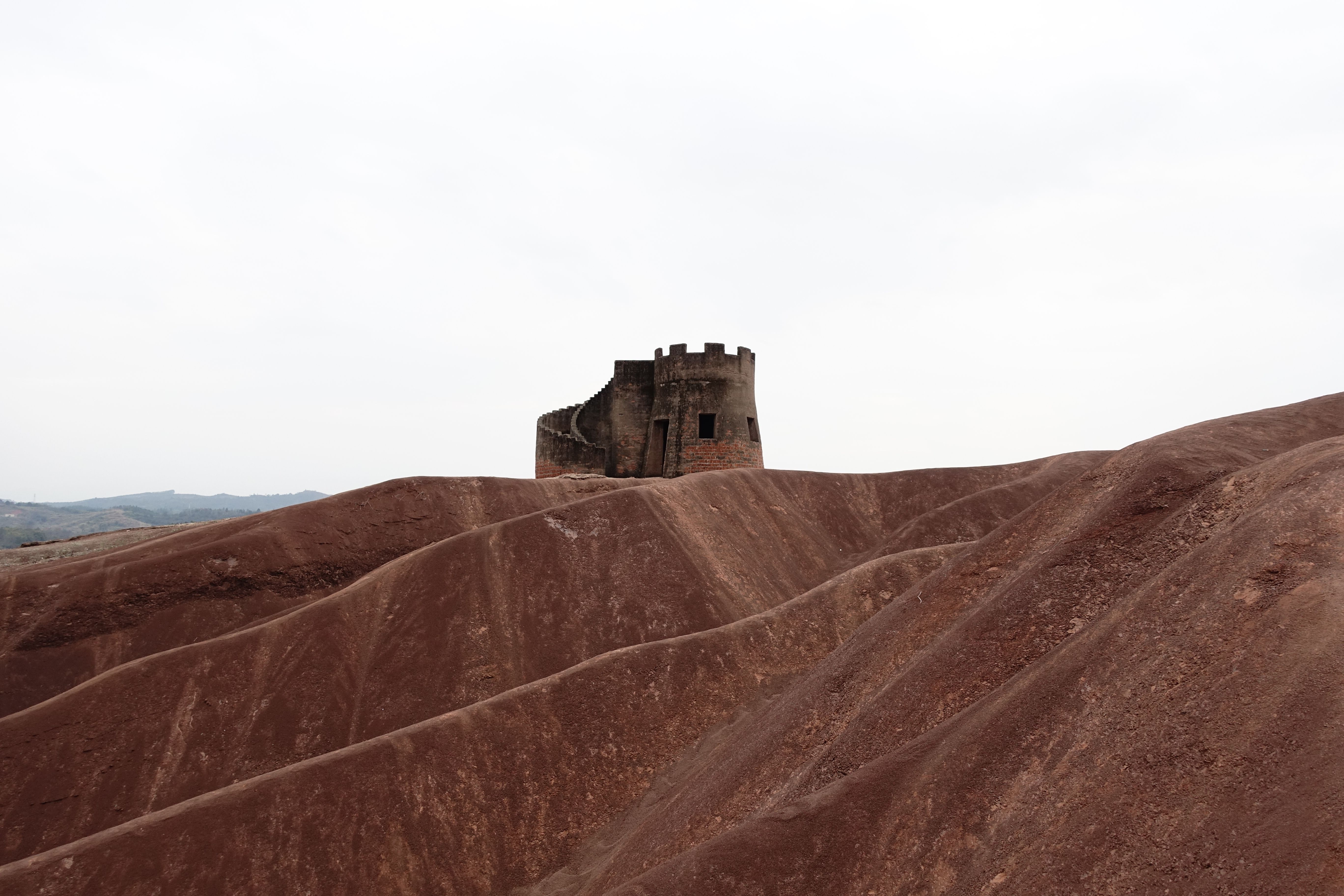 A historic tower stands amidst rugged desert hills, showcasing striking geological formations.