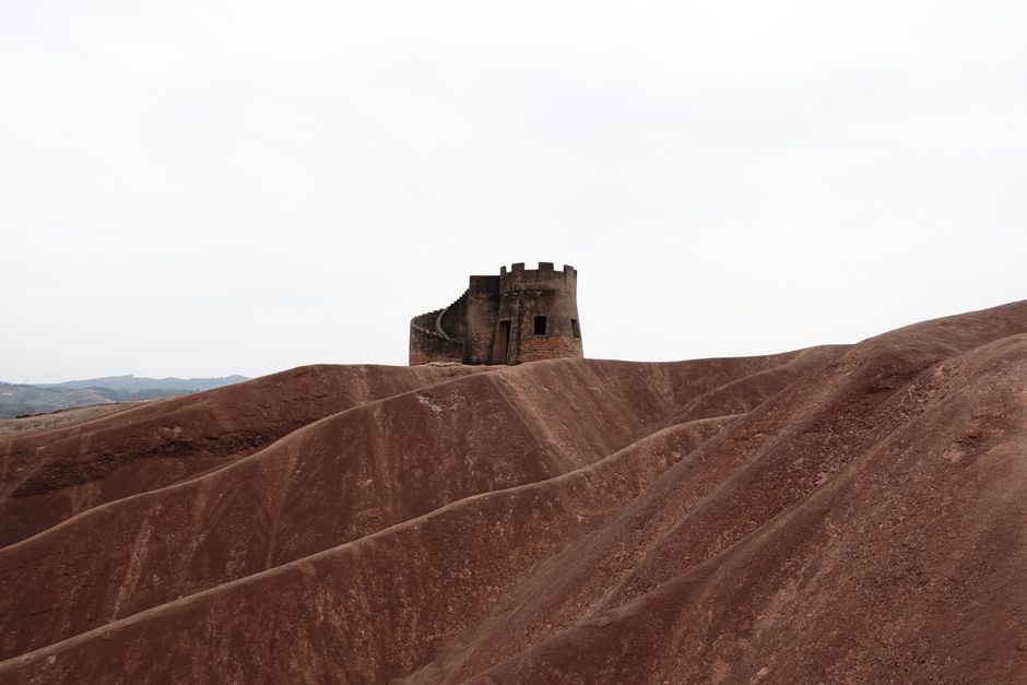 A historic tower stands amidst rugged desert hills, showcasing striking geological formations.