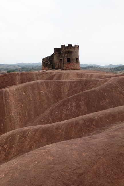 Ancient fortress tower standing on eroded, wave-like red clay formations.
