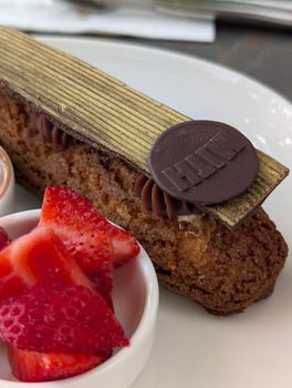 Luxurious chocolate eclair topped with chocolate disc and straw slices, ready to indulge.