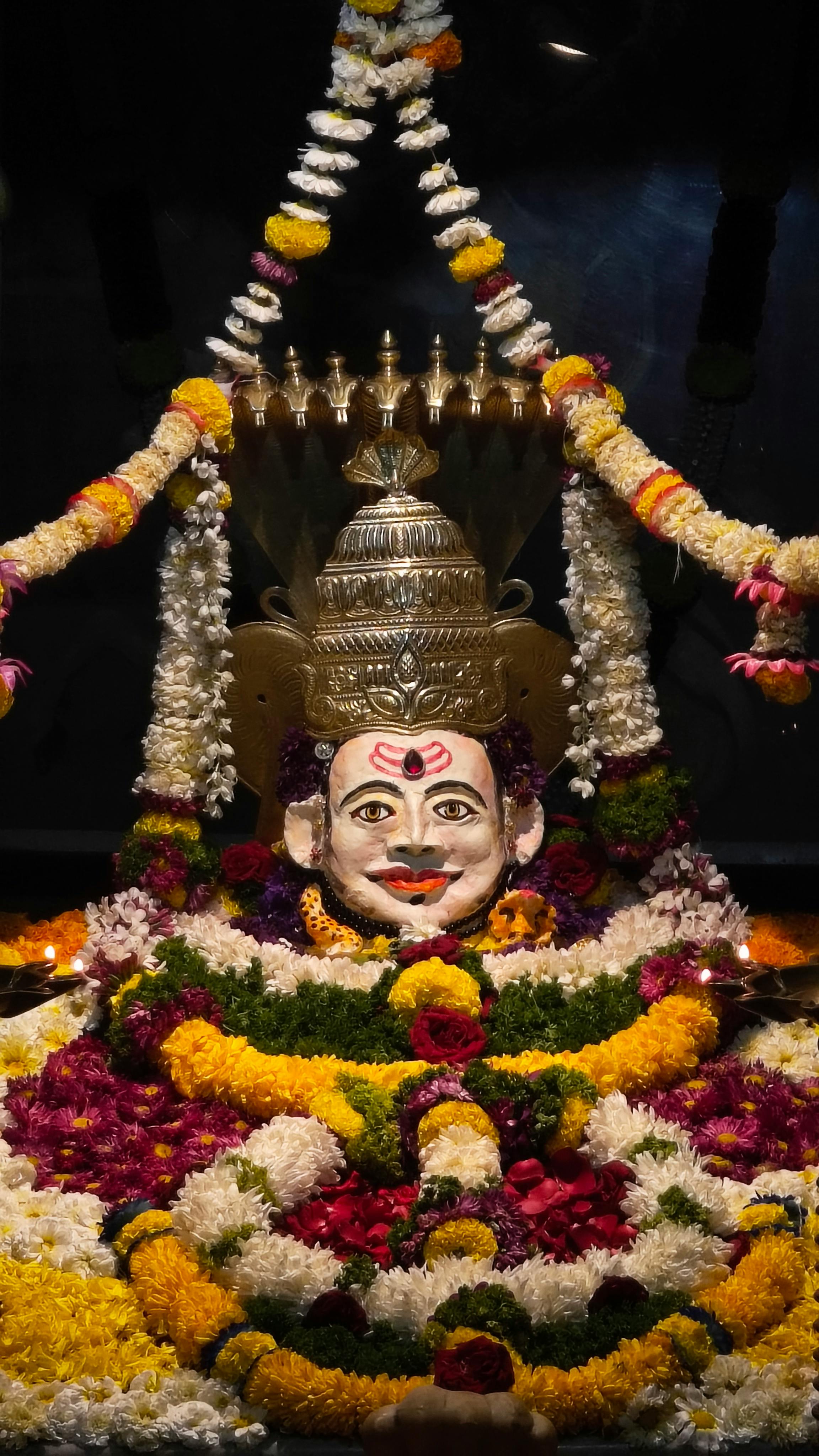 Colorful floral decoration surrounding a Hindu idol in a temple setting.