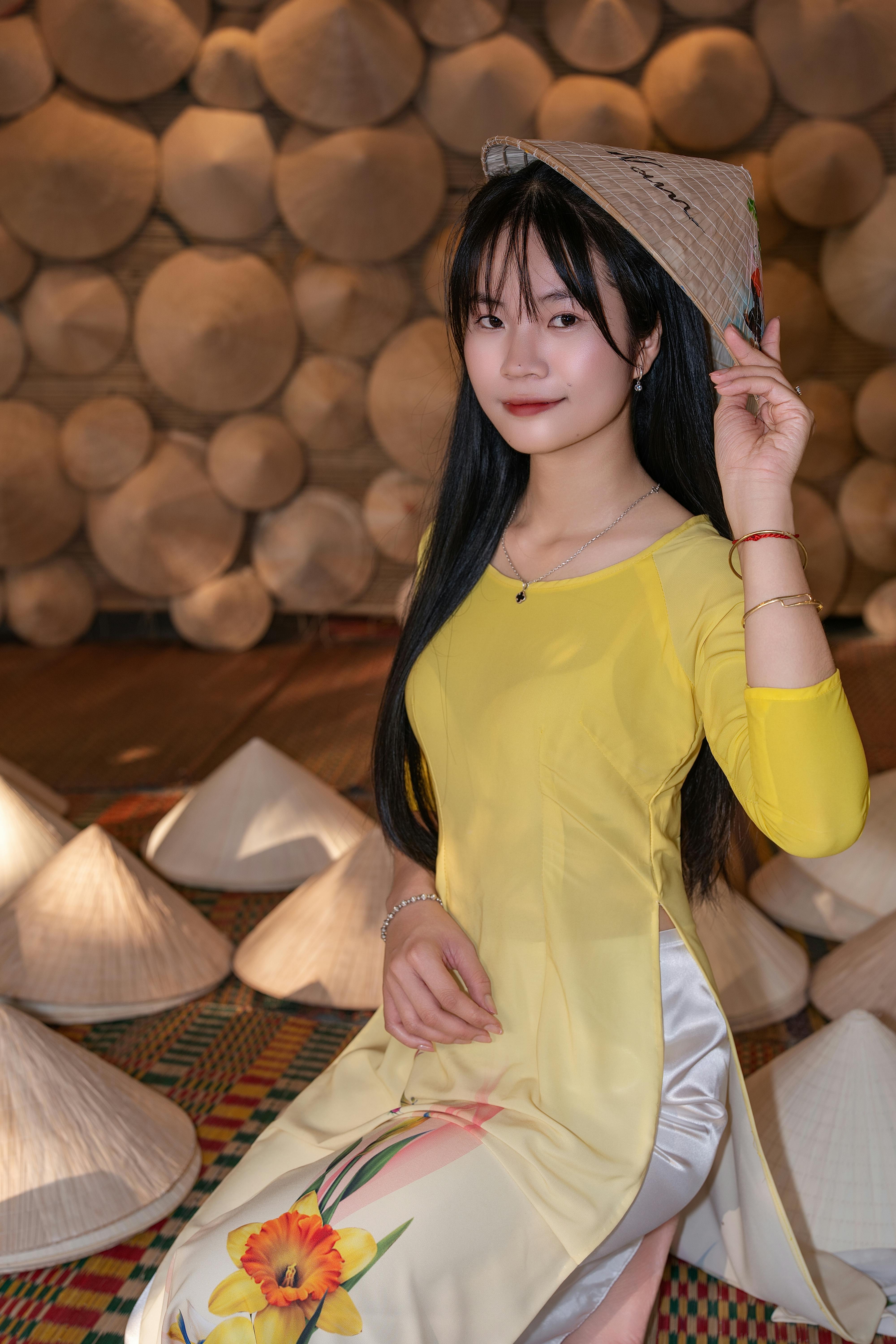 Woman in yellow áo dài posing with a conical hat in a cultural setting.