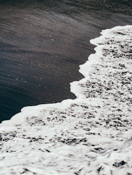 Serene view of ocean waves flowing onto a black sand beach, creating a calming contrast.