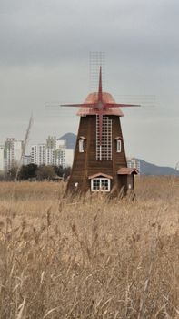 A rustic windmill stands in a golden field with a cityscape in the background.