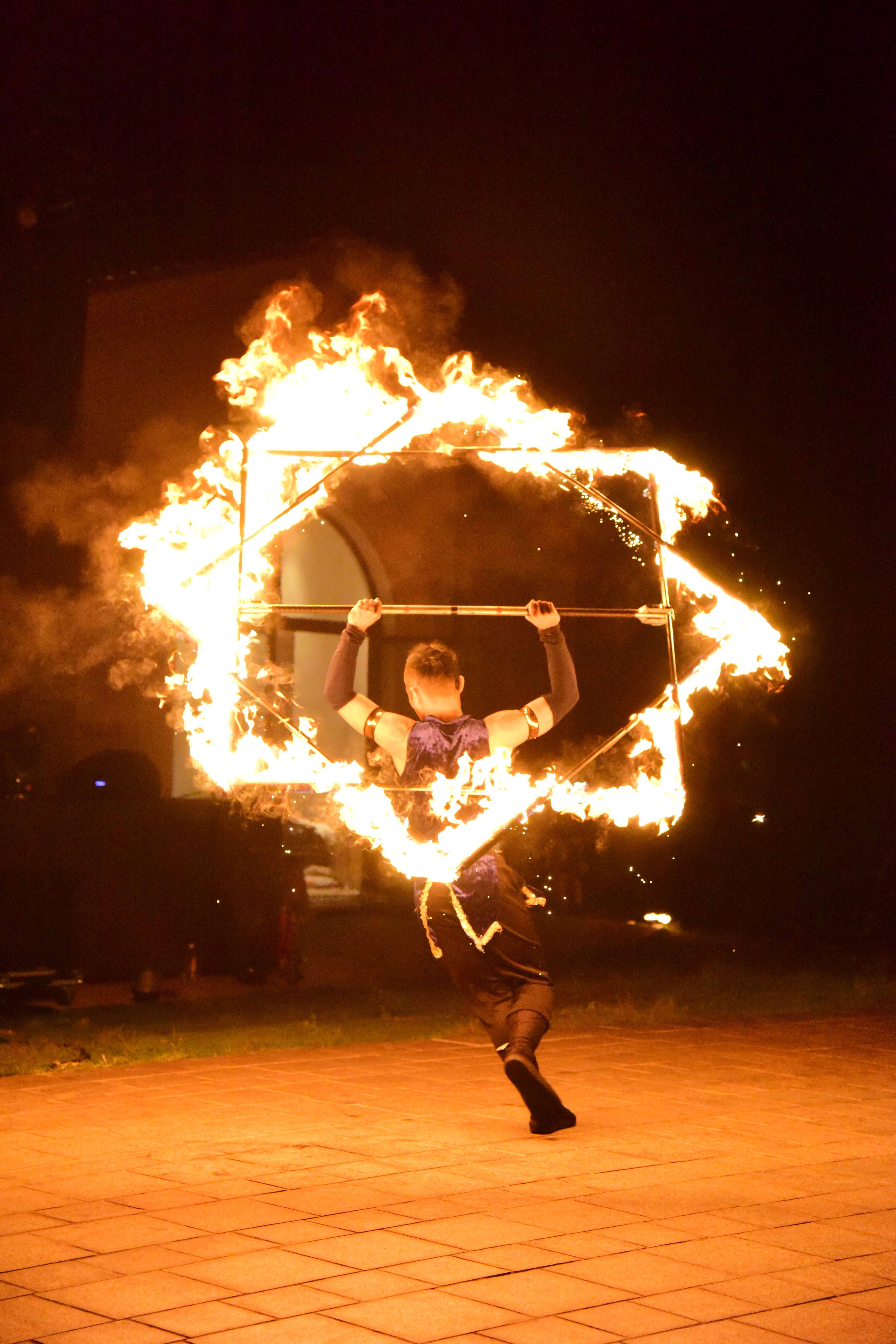 Dramatic night scene of a fire performer manipulating a flaming cube outdoors.