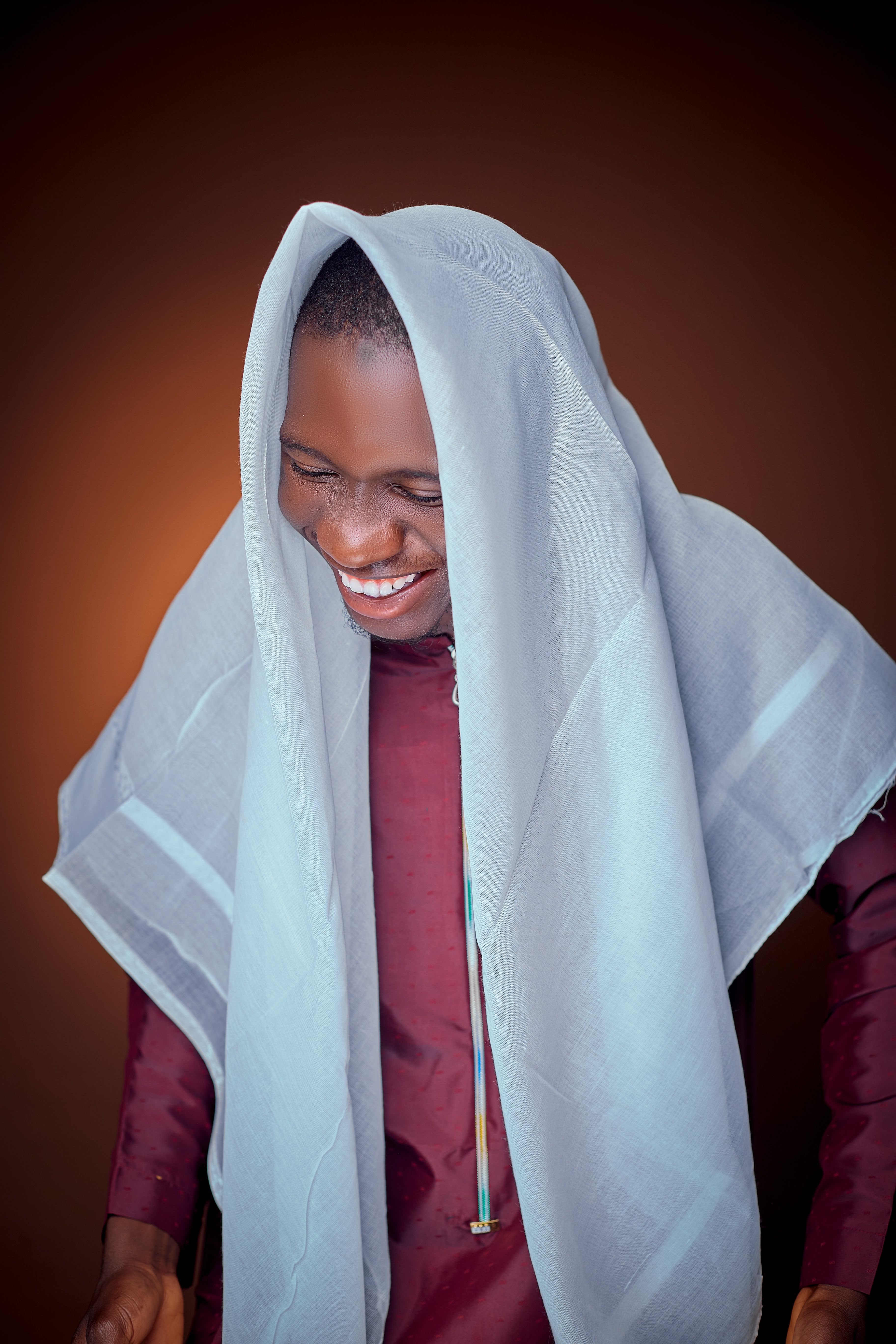 Portrait of a smiling man with white fabric draped over head, creating a hijab style look.