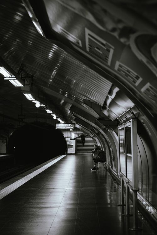 Free Black and white photo of a metro station with curved architecture and one person waiting. Stock Photo