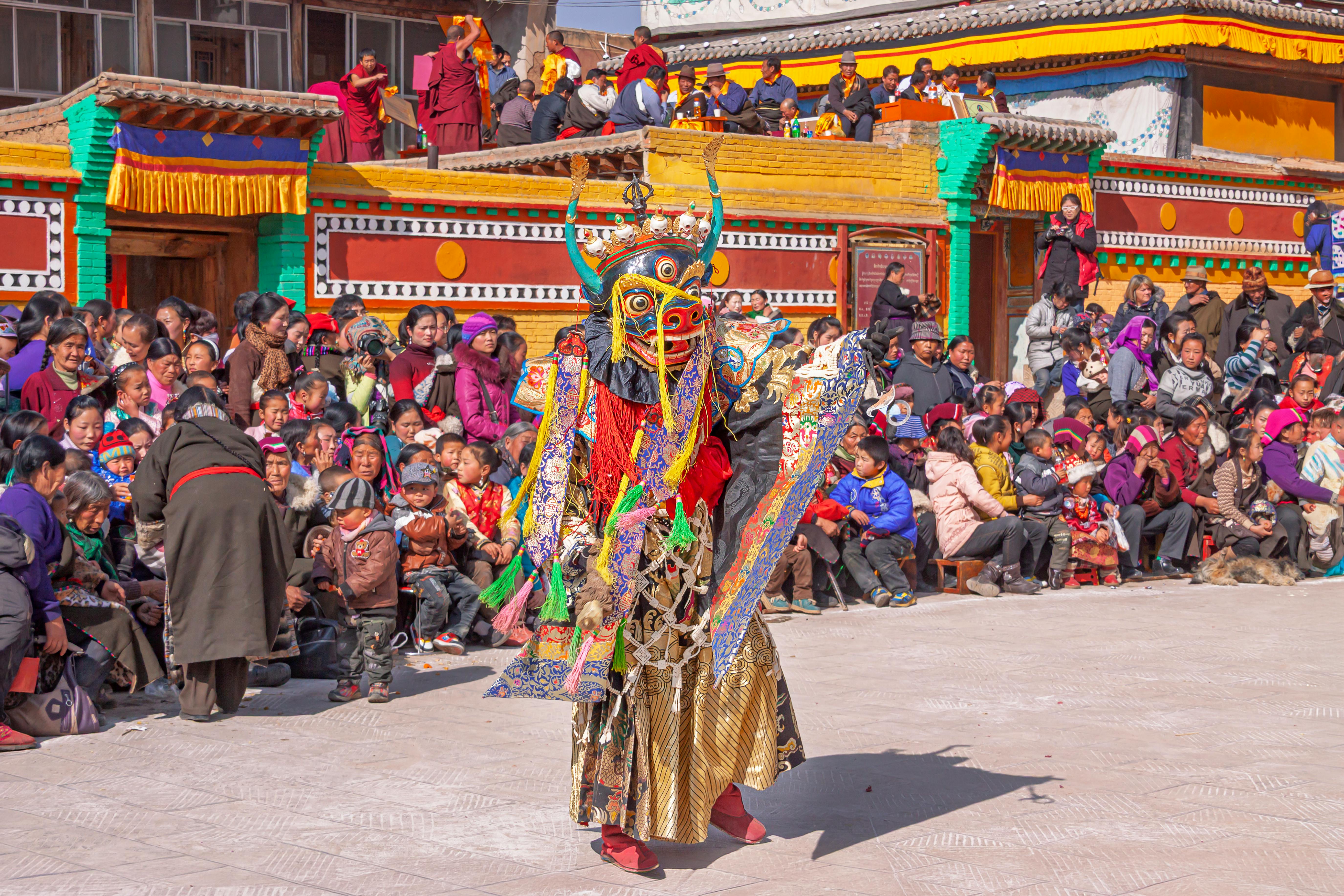 Traditional Tibetan masked dancer performing in front of a crowd at a vibrant festival in Huangnan, China.