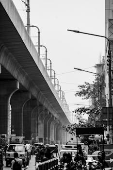 A bustling urban street scene with an elevated metro track, captured in black and white.