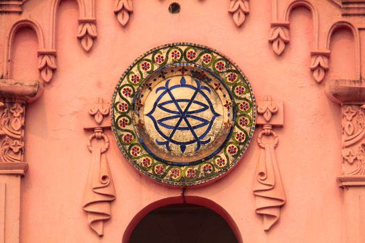 Close-up of ornate circular design on pink temple wall, showcasing traditional artistry.