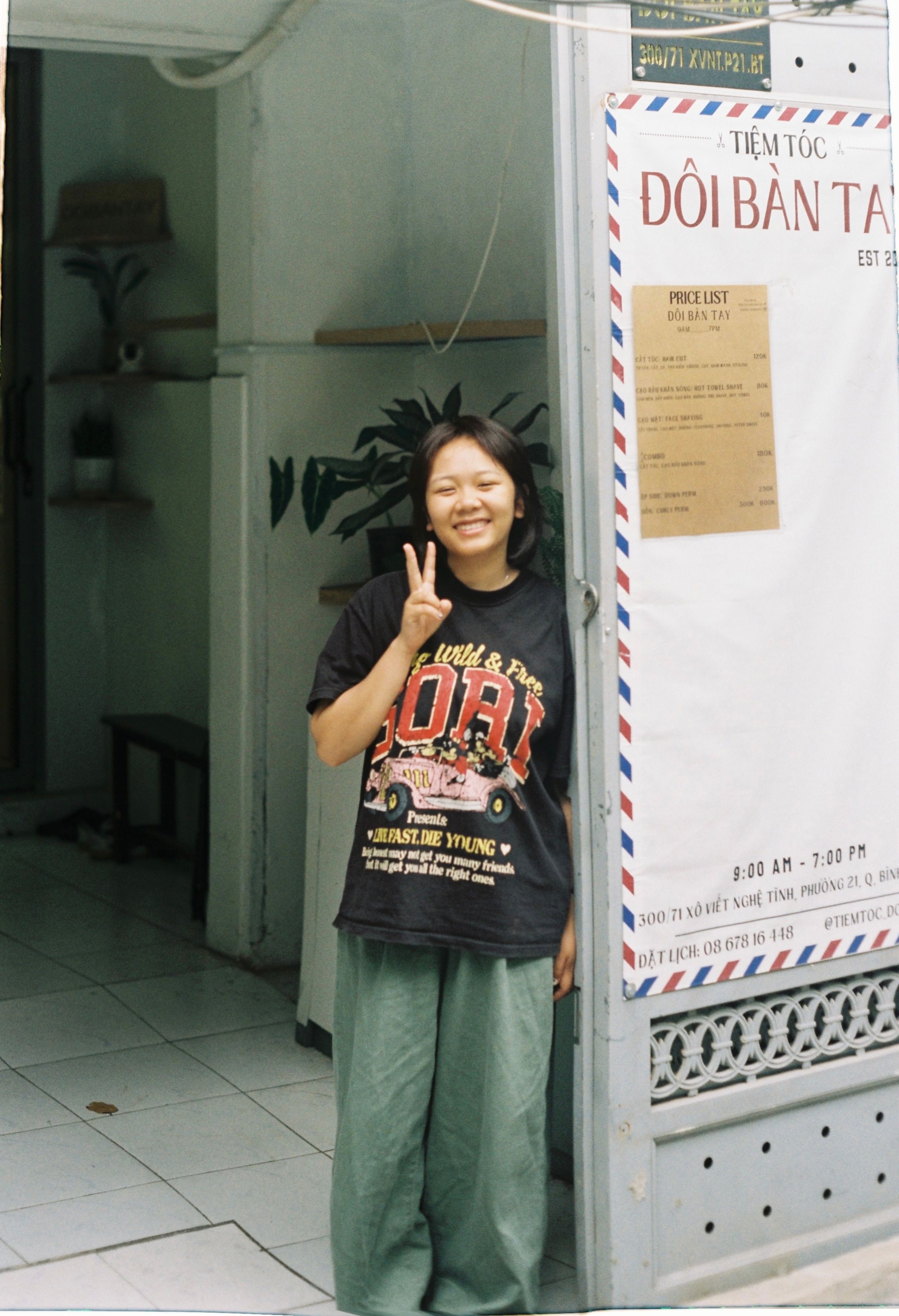 Woman posing with peace sign at a shop entrance, exuding happiness.