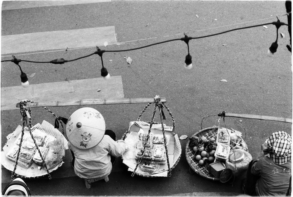 Black and white image of street vendors selling food with conical hats, taken from above.